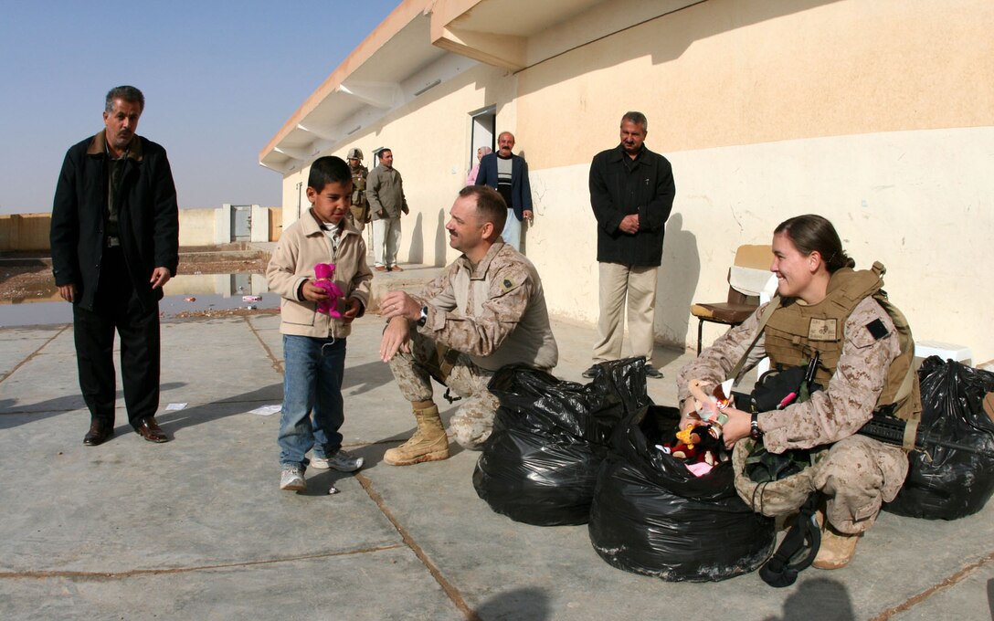 At Mekasid Primary School in Rutbah, Iraq, 1st Sgt. Clark Rhiel (center), the company first sergeant for Headquarters and Service Company, 2nd Battalion, 25th Marine Regiment, Regimental Combat Team 5, and Petty Officer 2nd Class Bridget Shanahan, a corpsman with Shock and Trauma Platoon, 2nd Combat Logistics Battalion, pass out toys to students Dec. 23. The Marines and sailors also brought snacks and soccer balls to the students. ::r::::n::