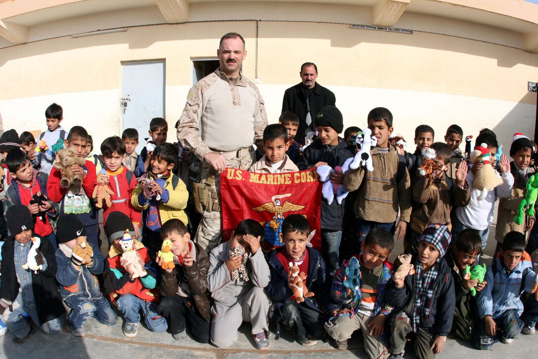 First Sgt. Clark Rhiel (center), the first sergeant for Headquarters and Service Company, 2nd Battalion, 25th Marine Regiment, Regimental Combat Team 5, gathers second grade students for a photo with the Marine Corps flag at Mekasid Primary School in Rutbah, Iraq, Dec. 23.  After distributing toys, snacks and soccer balls to the students, the Marines had the school principal sign the flag, which they mailed to the citizens of Medina, Ohio, who donated and mailed the items to Iraq in early December.   ::r::::n::