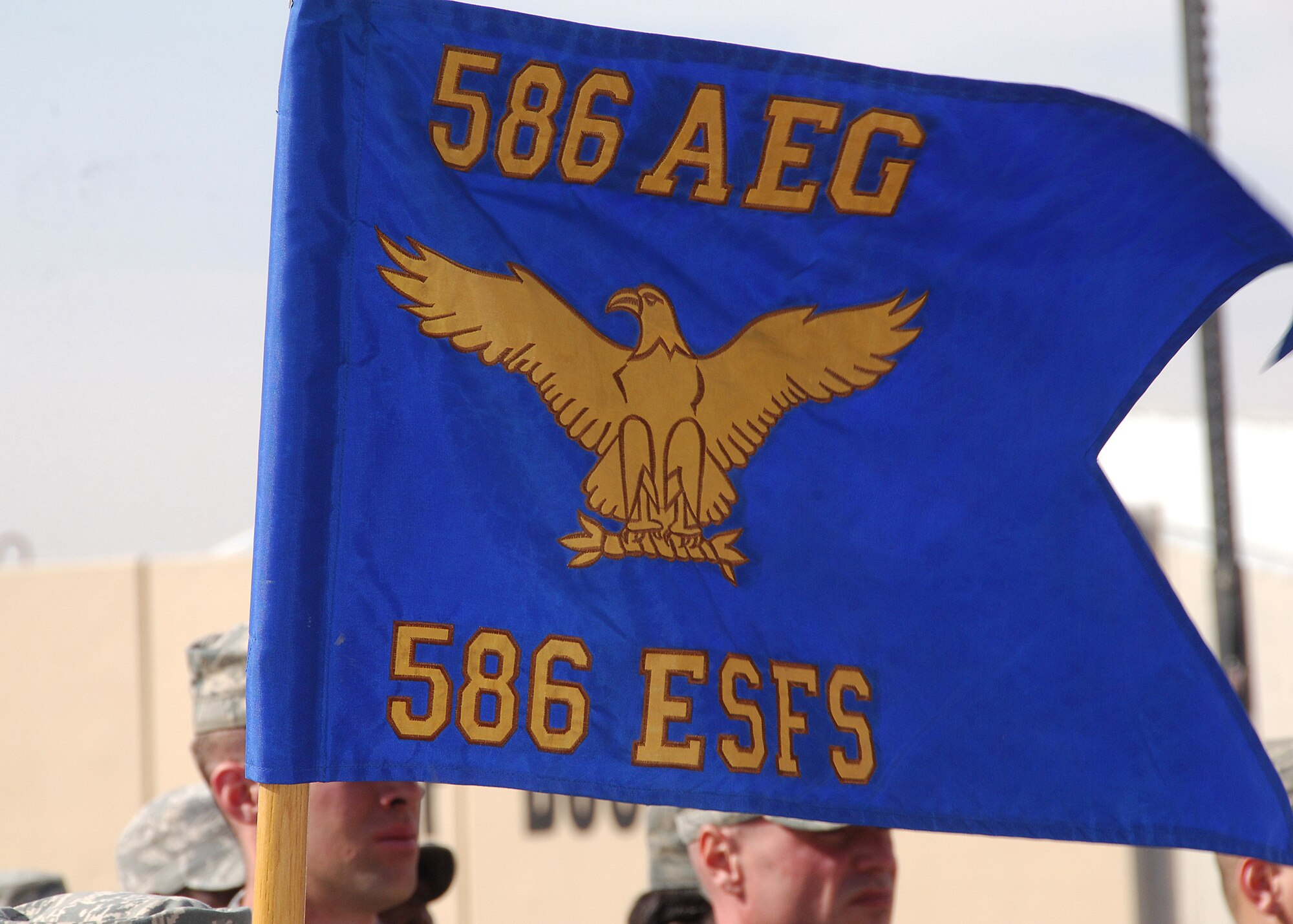 CAMP BUCCA, IRAQ -- The flag of the 586th Expeditionary Security Forces Squadron flies proudly while its members stand in formation during the unit's inactivation ceremony on Dec. 22. During its tenure, the 586th ESFS provided detainee operations and forward operating base defense, and conducted area security operations while providing convoy security for almost four years. The different mission sets of the 586th ESFS will now be handled by the 887th ESFS and Ugandan military members. (U.S. Air Force photo/Tech. Sgt. Raheem Moore)