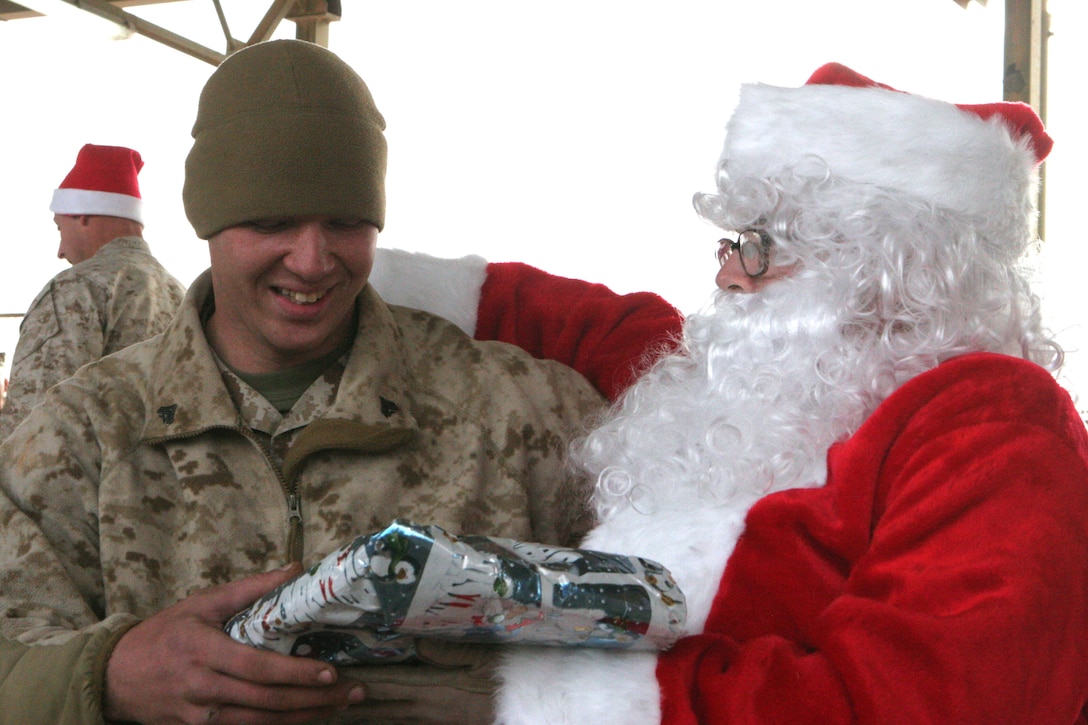 Cpl. Joshua A. Mendenhall, 23, Kansas City, Mo., motor transportation mechanic, Transportation Security Company, Combat Logistics Battalion 2, 1st Marine Logistics Group, receives a present from Santa Claus here Dec. 25. Two-hundred and fifteen Marines and Sailors each received a gift that was donated by family members and friends of the family of Capt. Tim P. Maloney, commanding officer, TS Co., CLB-2, 1st MLG. ?Being away from friends, family and home isn?t easy,? said Maloney, 30, Milton, Mass. ?To brighten up their Christmas, my wife Christina started coordinating and collecting donated gifts to send out here to the Marines and Sailors.? The platoon commanders of TS Co. collected a wish list from their troops to send back to the U.S. in November so the present would make it here by Christmas. ?Overall it shows that the people back home still truly care about the service members and what they do for our country.?