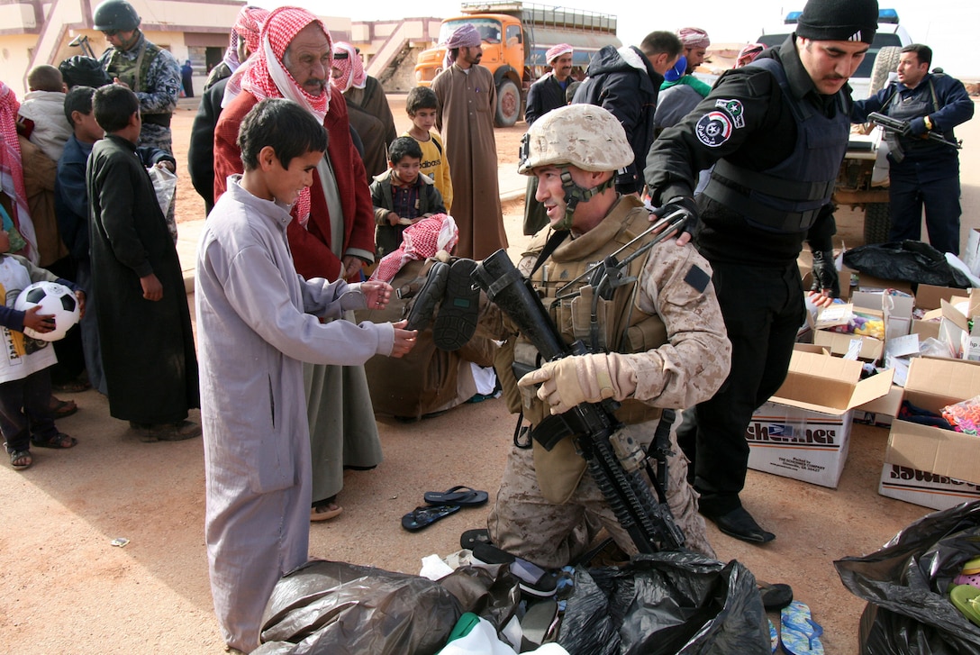 Alongside Iraqi police officers, Sgt. Christopher Bambury, a team leader with Weapons Company, 2nd Battalion, 25th Marine Regiment, gives a pair of shoes to an Iraqi boy during a distribution of clothing and other supplies to Bedouin families in Walej, Iraq, Dec. 26.  In an effort to foster community policing in accordance with their security line of operations strategic objective, Marines teamed up with Iraqi Police based near the Port of Waleed, on Iraq’s border with Syria, to bring hundreds of pounds of clothing and other items to the impoverished people of the town in preparation for winter.  ::r::::n::Official USMC photo by Capt. Paul L. Greenberg::r::::n::