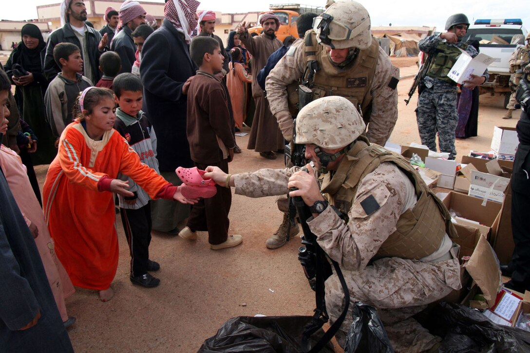 Sgt. Christopher Bambury, a vehicle commander with Weapons Company, 2nd Battalion, 25th Marine Regiment, Regimental Combat Team 5, gives a pair of shoes to an Iraqi girl during a distribution of clothing and other supplies to Bedouin families in Walej, Iraq on Dec. 26.  Bambury, a Reserve Marine on his second tour in Iraq, is also a New York City firefighter from Breezy Point, N.Y.  More than 60 pair of shoes were collected and mailed to Bamburyâ??s unit in Iraq by a teacher and students from a Long Island, N.Y. middle school.::r::::n::