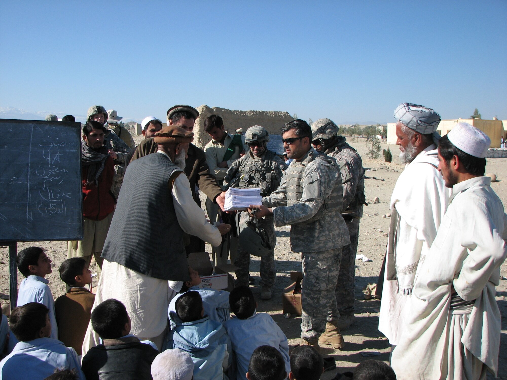 An interpreter with the Nangarhar Provincial Reconstruction Team passes a package of paper to a teacher at a school in Terelay village in Chaparhar District.  Members of the PRT, along with the Chaparhar Police Mentor Team, met with village elders before passing out school supplies to children and teachers at the school. (Photo by Capt. Dustin Hart)
