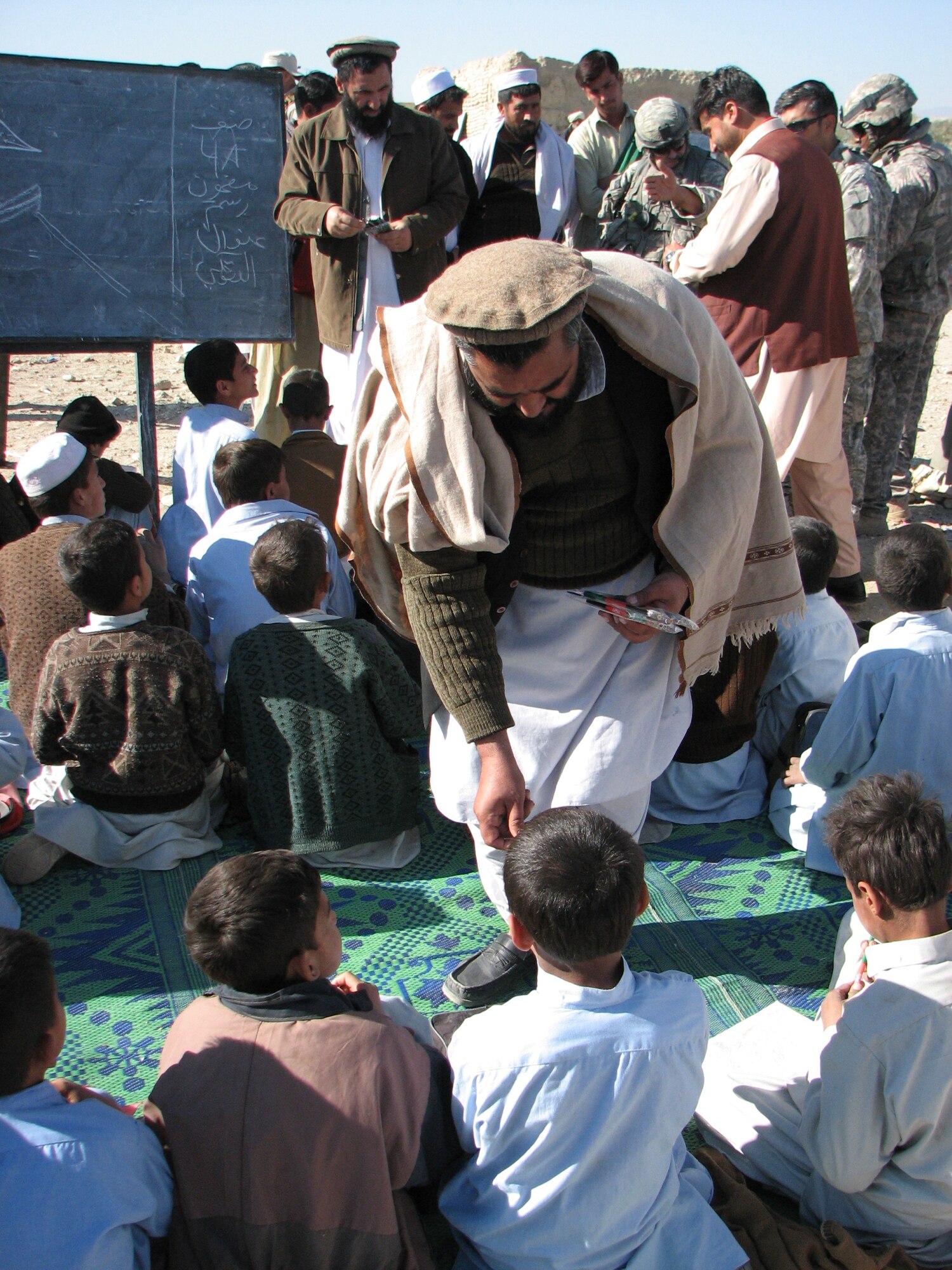 A village elder hands out pencils to children at a school in Terelay Village, Chaparhar District, Dec. 24.  The pencils were provided by the Nangarhar Provincial Reconstruction Team and Chaparhar Police Mentor Team, who were visiting with the elders at the school. (Photo by Capt. Dustin Hart)
