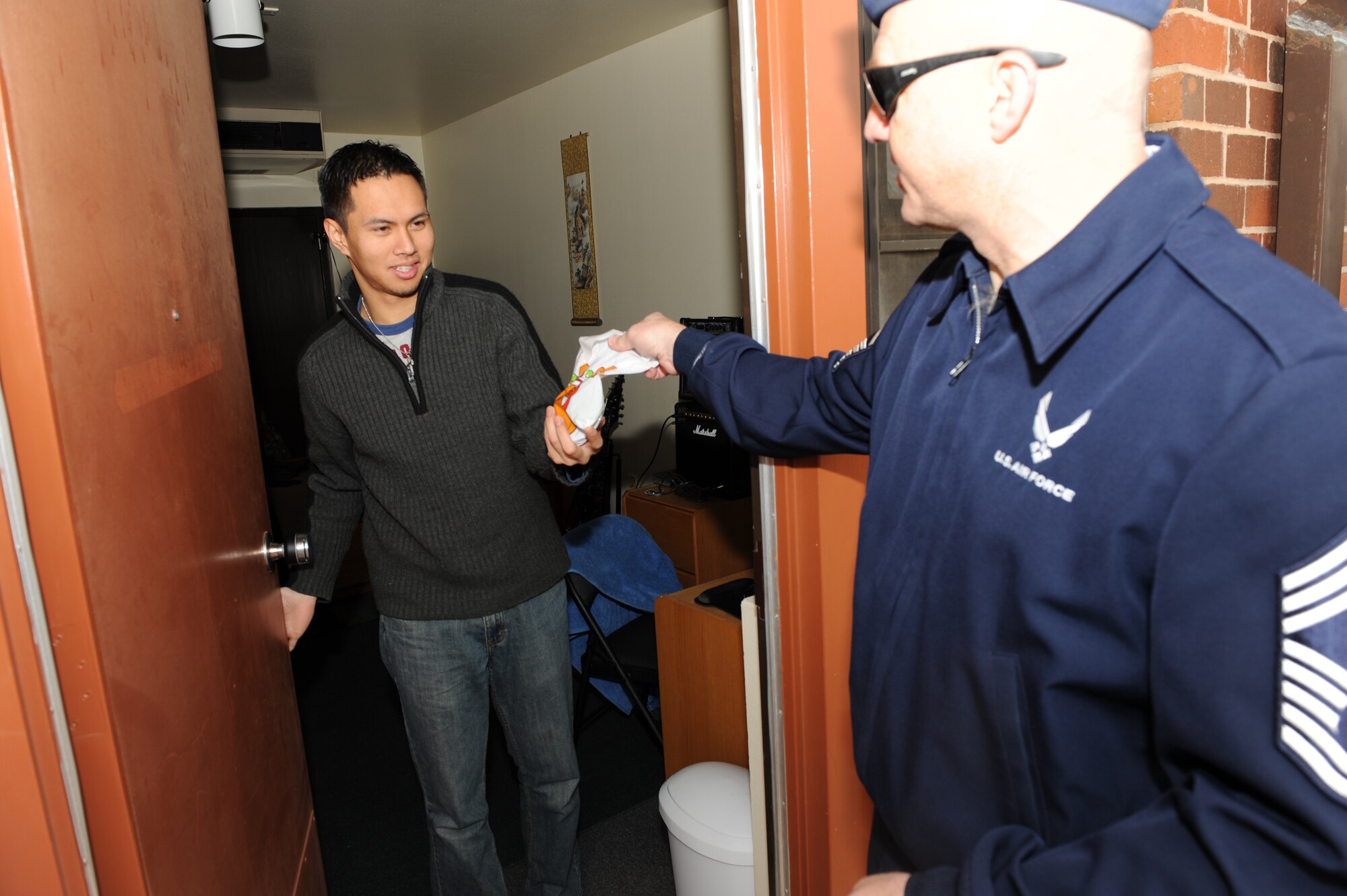 DYESS AIR FORCE BASE, Texas -- Chief Master Sgt. Kenneth Simonton, 7th Aircraft Maintenance Squadron first sergeant, delivers cookies to dormitory resident Airman 1st Class Ivan Deleon, 7th Medical Group, Dec. 20. The first shirts collect cookies every December to "drop" to Airmen who may be away from home during the holidays. (U.S. Air Force photo/Staff Sgt. Connor Estes)