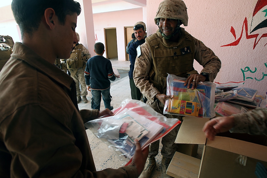 Sgt. Maj. Wallington D. Sims, sergeant major, Company A, Marine Wing Support Squadron 373, 1st Marine Logistics Group, hands out school supplies during a humanitarian mission here Dec. 30. Sims, 46, St. Louis, and other Marines from 1st MLG visited Habbaniyah Tourist Village?s public school to donate school supplies on behalf of Operation Iraqi Children, a nonprofit organization that, according to the official mission statement, ?allows Americans to send school supply kits and other necessities to Iraqi children.?