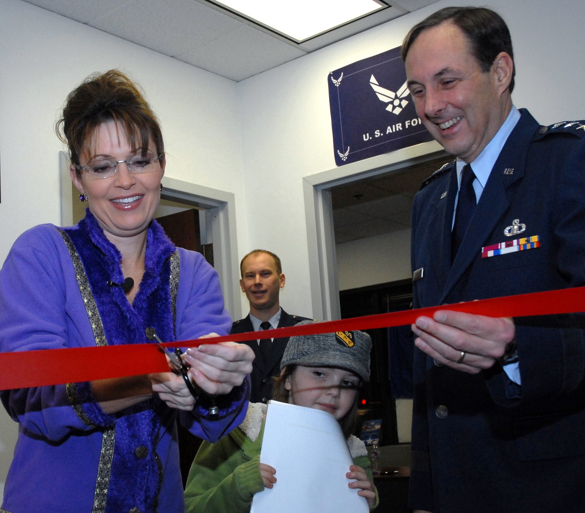 Alaska Governor Sarah Palin, commander-in-chief of the Alaska Air National Guard, cuts the ribbon at the opening of the guard's new Valley Recruiting Office Dec. 22, 2008, while daughter Piper, 7, looks on. A joint venture between the Alaska National Guard and the active-duty Air Force, the new office is the guard's first-ever full-time presence in the Mat-Su Valley. Assisting the governor is Lt. Gen. (Alaska) Craig Campbell, adjutant general of the Alaska National Guard. In the background is Maj. Ed Soto, commander of the 176th Wing's Civil Engineer Squadron. Alaska National Guard photo by 2nd Lt. John Callahan.