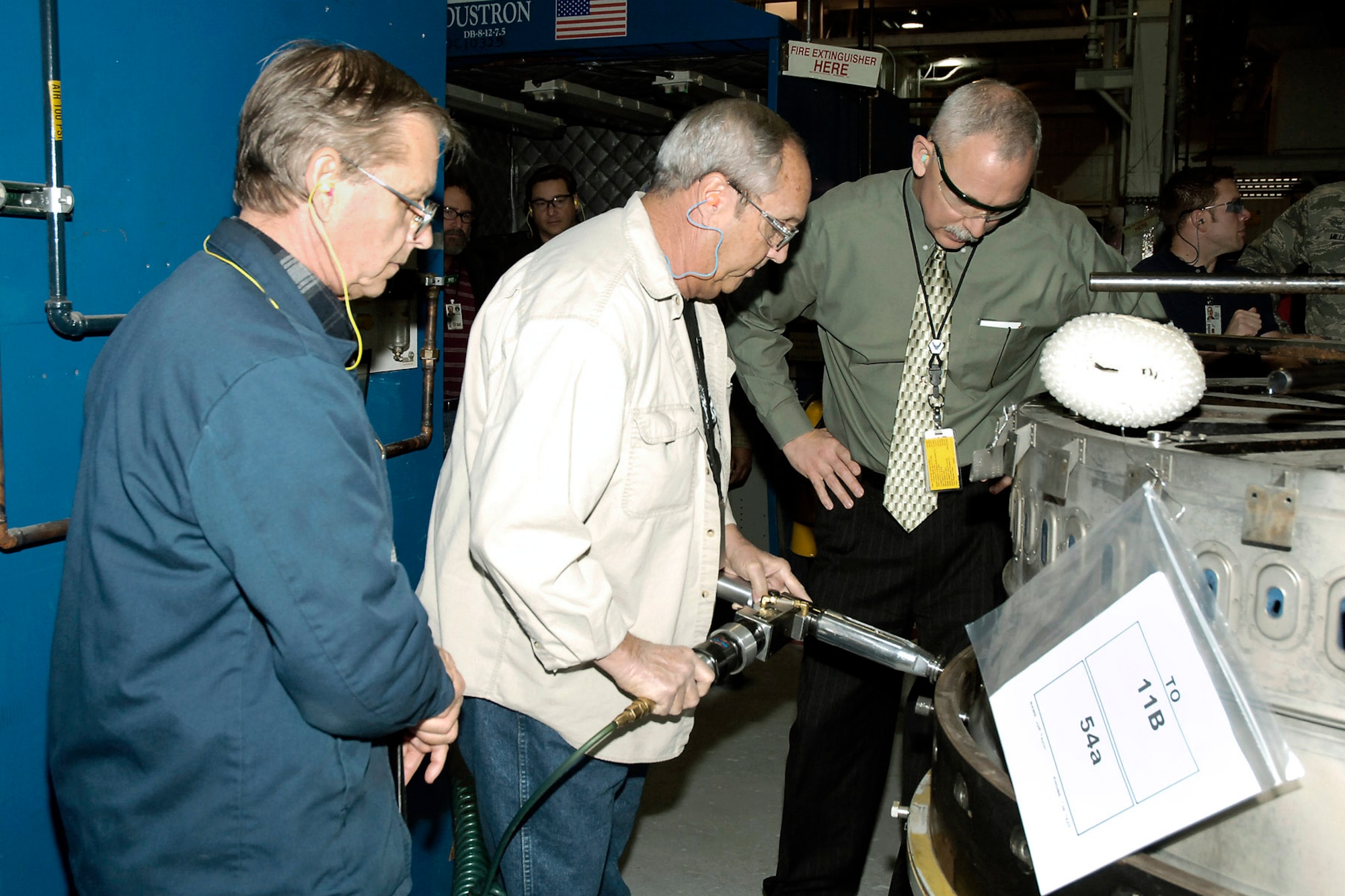 Design engineer Tom Pence (left) and drill operator Jerry Heiskill (middle) show Oklahoma City Air Logistics Center Executive Director John Over the improved process for drilling a duct-liner at Tinker Air Force Base, Okla. Mr. Pence and Mr. Heiskill are part of a team that combined a process improvement and safety improvement to save the Air Force time and money. (U.S. Air Force photo) 
