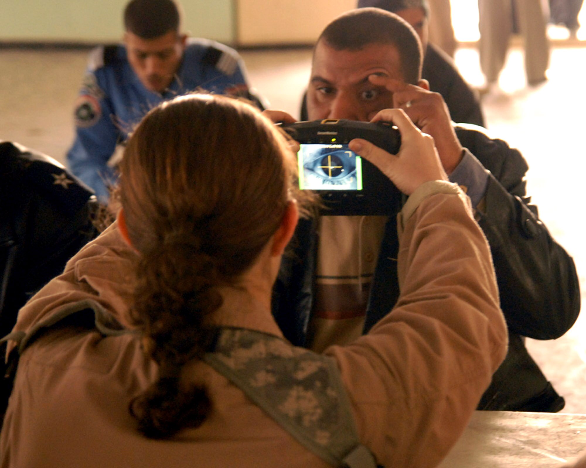 Airman 1st Class Amanda Houser takes an eye iris scan on an Iraqi policeman during the Hy al Amil Iraqi Police and Patrol Station's monthly pay day activities Jan. 30 the at Joint Security Station Black Lion in Baghdad, Iraq. The pay day activities included: a security search, being identified by an eye iris scan, showing the proper identification, and verifying the IP had their assigned weapons. Verifications were made with the help of U.S. expeditionary security forces.  Airman Houser is a native of Hortonville, Wis., and a member of Det. 3 of the 732nd Expeditionary Security Forces Squadron, 716th Military Police Battalion, 18th Military Police Brigade. (U.S. Army photo/Sgt. Daniel Blottenberger) 
