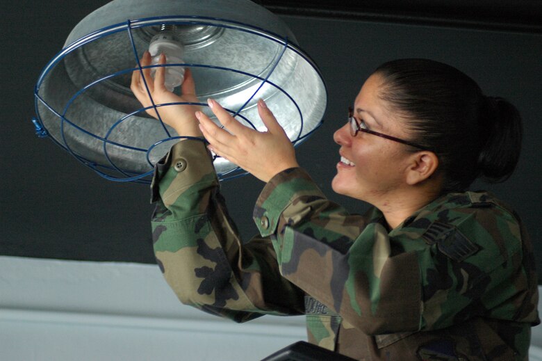 Staff Sgt. Maria Badure, Noncommissioned Officer in Charge of the 388th Maintenance Operations Squadron commander's support staff, installs an energy efficient, fluorescent light bulb in the wing pilot gym Feb. 6. 75th Civil Engineering initiated the switch, which is expected to save Hill Air Force Base $450 each year in energy costs.