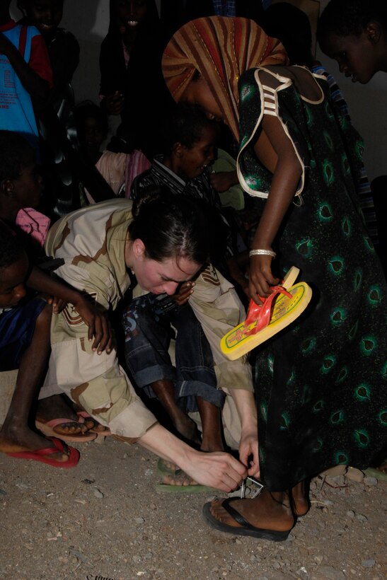 TSgt Victoria Bruyette helps a Djiboutian girl with her new flip-flops.  USAF Photo by SSgt Christina Styer