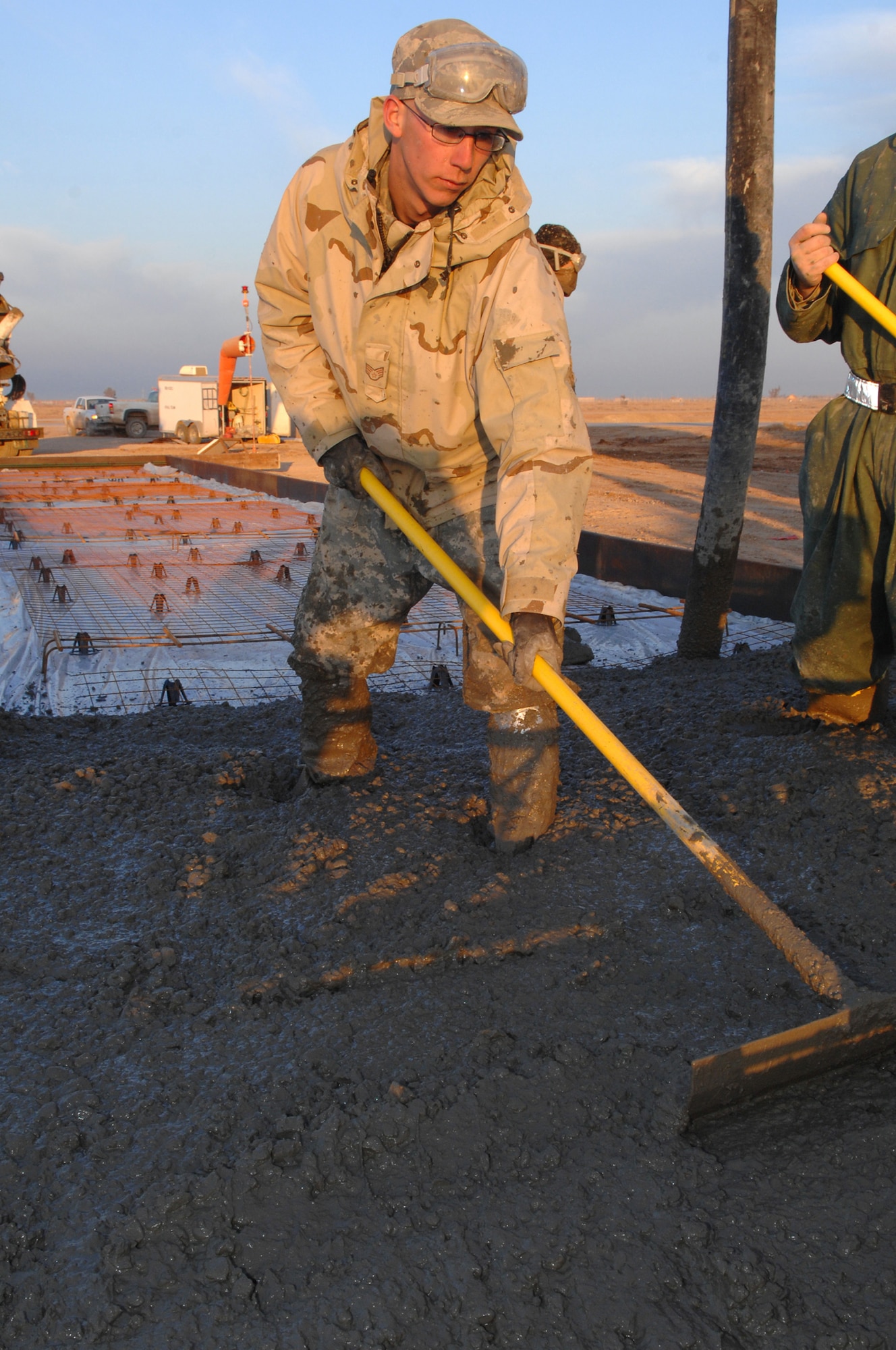BALAD AIR BASE, Iraq -- Senior Airman Jonathan Kidwell, one of the 332nd Expeditionary Civil Engineer Squadron pavement and heavy equipment flight's Dirt Boyz, spreads out concrete with a modified rake here, Feb. 6. Raking and pushing around the concrete helps to prevent bubbles and ensures that the pad is exactly one foot deep. Airman Kidwell is deployed from Peterson Air Force Base, Colo. (U.S. Air Force photo/ Senior Airman Julianne Showalter)