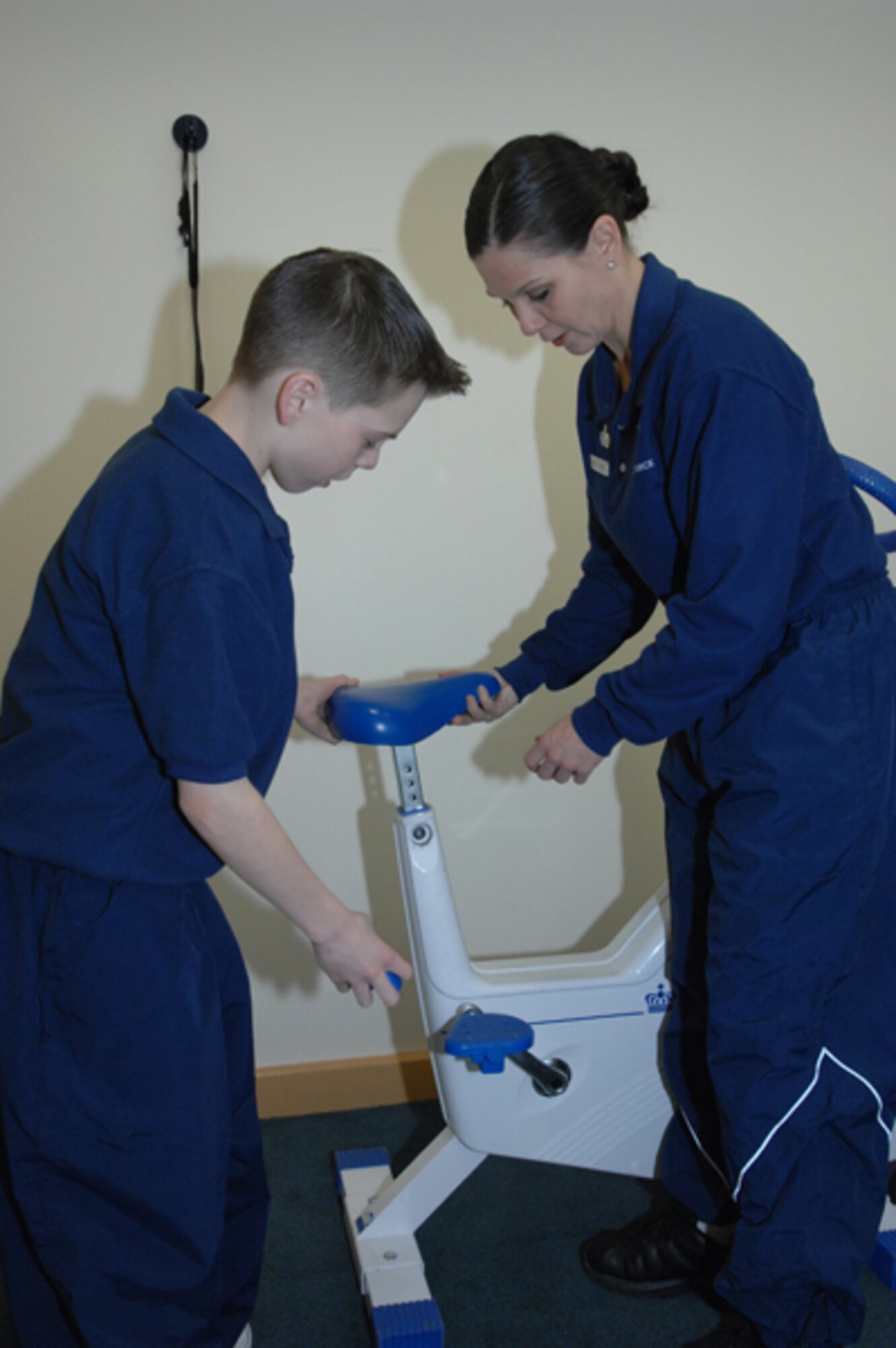 Master Sgt. Tammy Cope, 48th Services Squadron fitness center facility manager, shows her son, Josh, how to adjust the equipment used for the ergometry cycle testing Feb. 4 at the fitness center at RAF Lakenheath, England. Josh shadowed his mom at work as part of "Bring your Child to Work Day" at RAF Lakenheath. (U.S. Air Force photo by Staff Sgt. Vanessa Young)