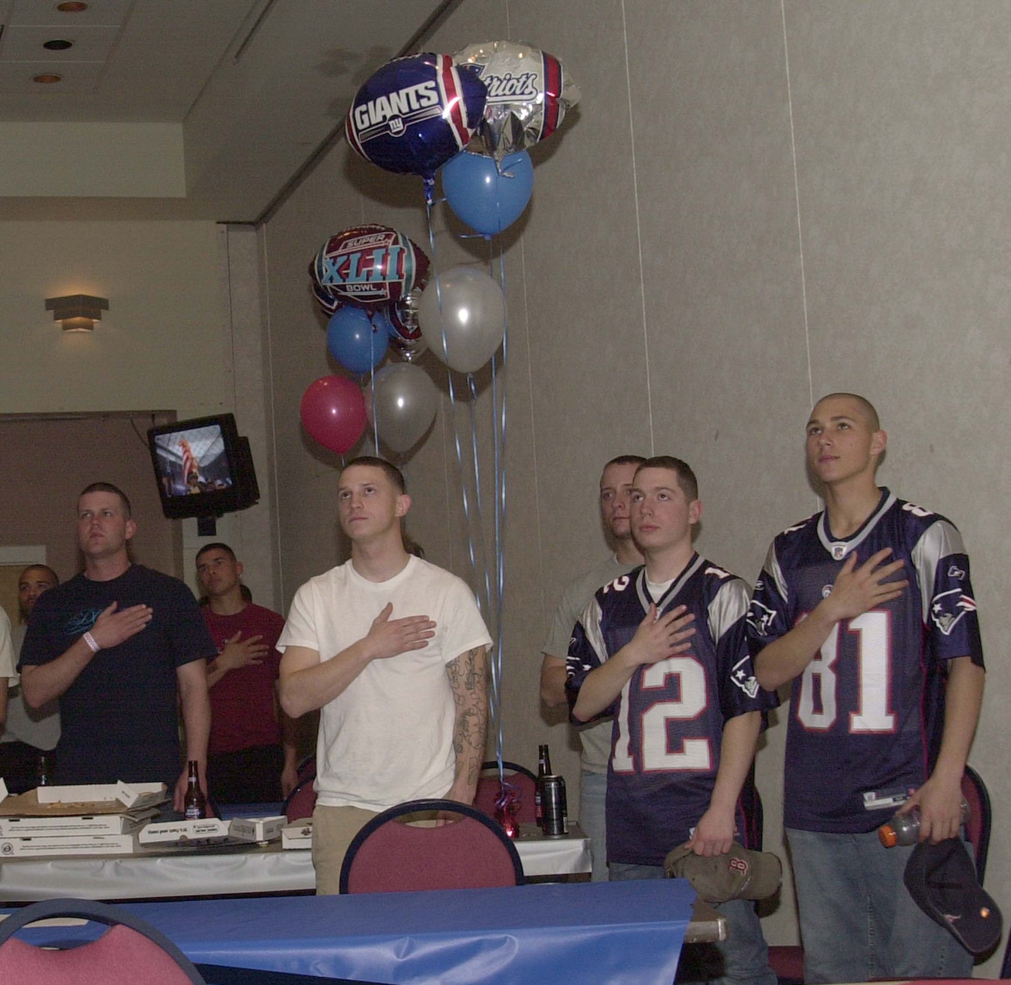 Guests at the Event Center place their right hands over their hearts as they listened to 2007 American Idol winner Jordin Sparks sing the National Anthem prior to the Super Bowl kick off. Balloons and sports memorabilia bearing the logos of the New York Giants and the New England Patriots were used as decorations through out the Events Center during the Super Bowl party Feb. 3. (U.S. Air Force photo by Senior Airman Luis Loza Gutierrez)