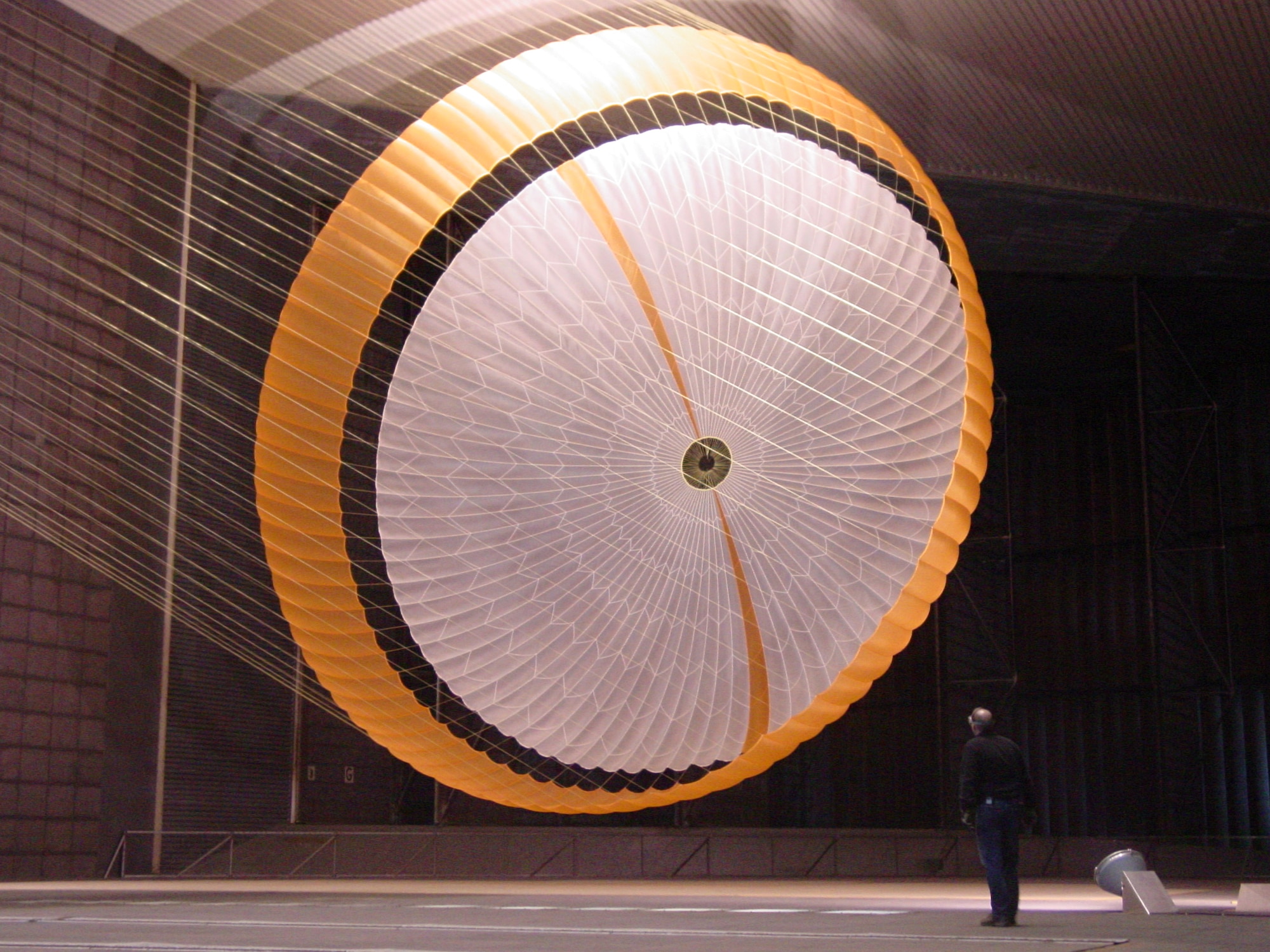 In this image, an engineer is dwarfed by NASA's Mars Science Laboratory's parachute, which holds more air than a 3,000-square-foot house and is designed to survive loads in excess of 36,000 kilograms (80,000 pounds). The parachute, built by Pioneer Aerospace, South Windsor, Conn., has 80 suspension lines, measures more than 65 feet in length, and opens to a diameter of nearly 55 feet. It is the largest disk-gap-band parachute ever built and is shown here inflated in the test section with only about 12.5 feet of clearance to both the floor and ceiling of the world’s largest wind tunnel at National Full-Scale Aerodynamics Complex. The parachute is attached to a launch arm mounted on a swivel-base that allows the test item to pitch and yaw under simulated conditions of subsonic entry into the Martian atmosphere. (Photo courtesy of NASA/JPL and Pioneer Aerospace Corp.)