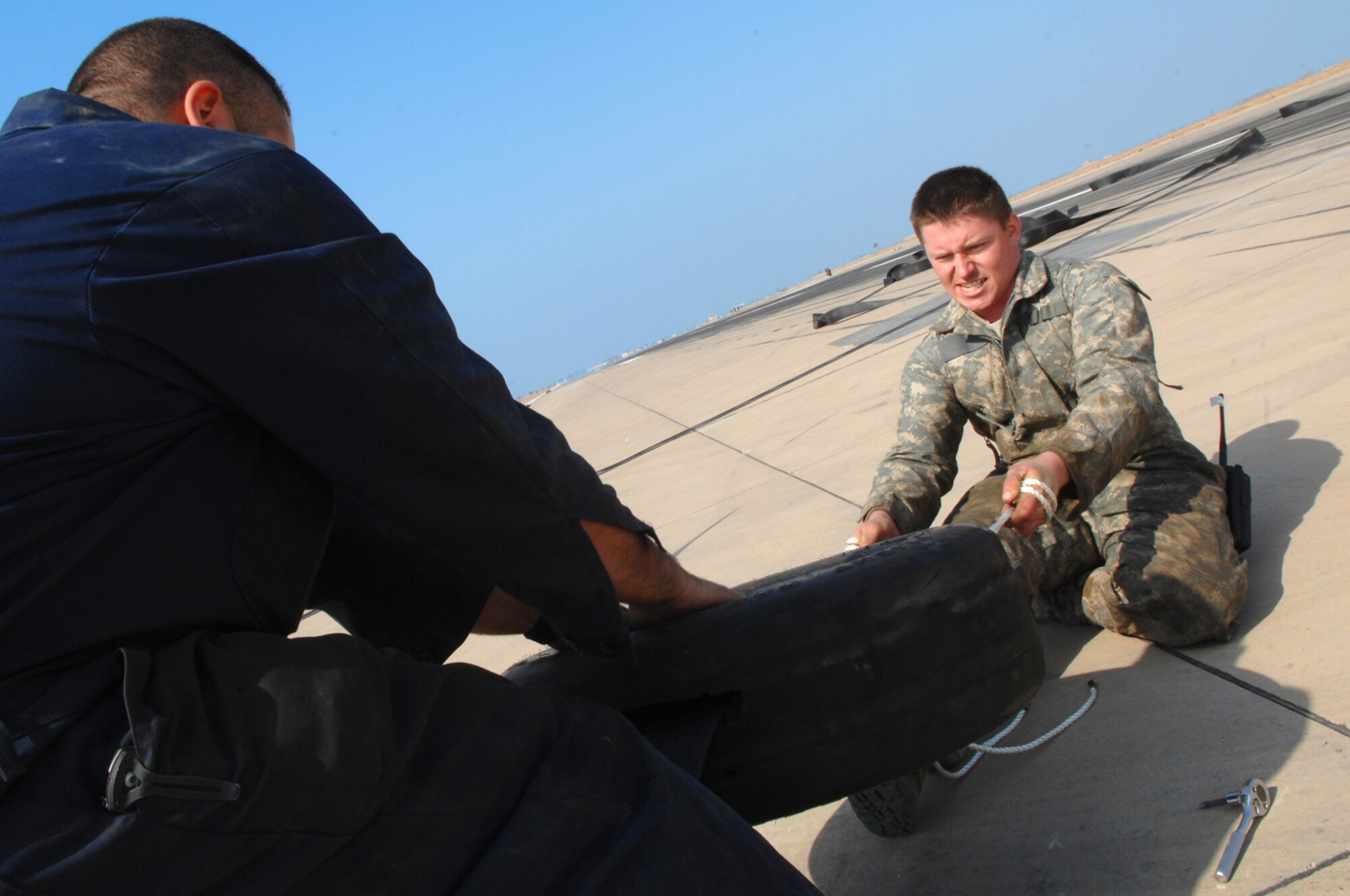 BALAD AIR BASE, Iraq -- Staff Sgt. Derrick Seals, 332nd Expeditionary Civil Engineer Squadron barrier system maintainer, pulls a tape connector through a tire here, Feb. 9. The tire protects the connector from wearing down over time because of friction. The emergency barrier system gives the Air Force the ability to launch aircraft and recover them anywhere in the world. Sergeant Seals is deployed from Eglin Air Force Base, Fla. (U.S. Air Force photo/ Senior Airman Julianne Showalter)
