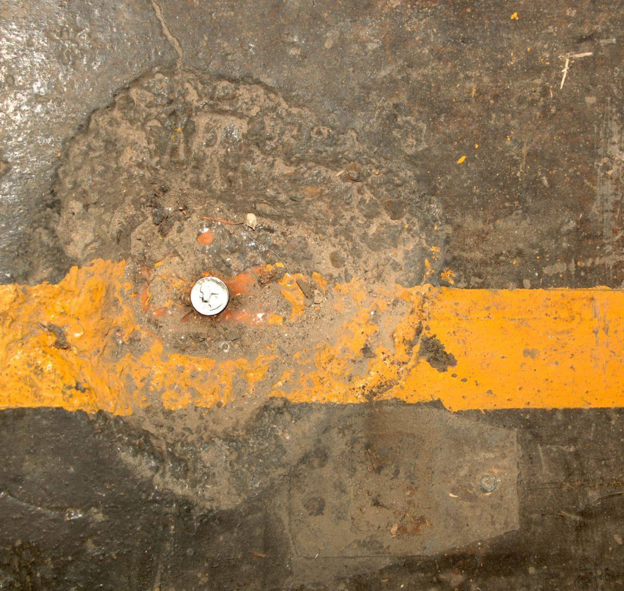 The damage from a 5 pound Royal Air Force practice bomb to the floor of the aircraft hanger at Molesworth on July 4th, 1944.  A U.S. quarter coin shows perspective on the approximaely 1 foot wide hole. The bomb was accidentially dropped by the RAF during a nighttime practice bombing sortie intended for a target field about 15 miles away.  (U.S. Air Force Photo by Staff Sgt. Jocelyn L. Rich)