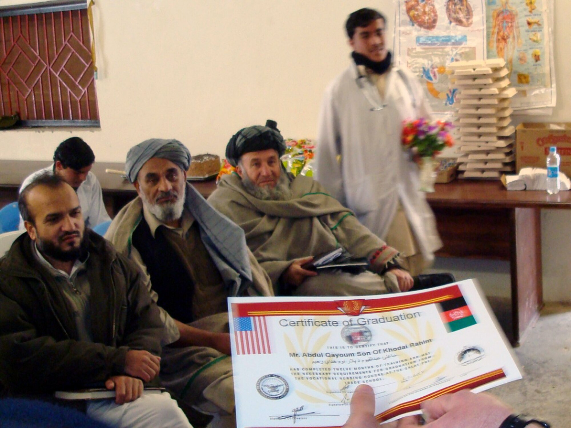 A graduate of the basic nursing program here hurries to the front of the room to accept his certificate of completion Feb. 5 as three dignitaries from Zabul Province look on.  The graduation ceremony was attended by (l to r) Director of Public Health Dr. Nazir Ahmadzai, Director of Education Mr. Abdul Nabi Wadan and Director of Ibn Sina Medical Dr. Fazul Rahman. The 12-month training program-facilitated by the joint Air Force and Army Provincial Reconstruction Team-teaches students the basics of nursing: taking vital signs, assessing overall health, initial patient screening, medical terminology and an overview of medications. The course is taught by a local Afghan employed by the PRT. (U.S. Air Force photo/Capt. Bob Everdeen)