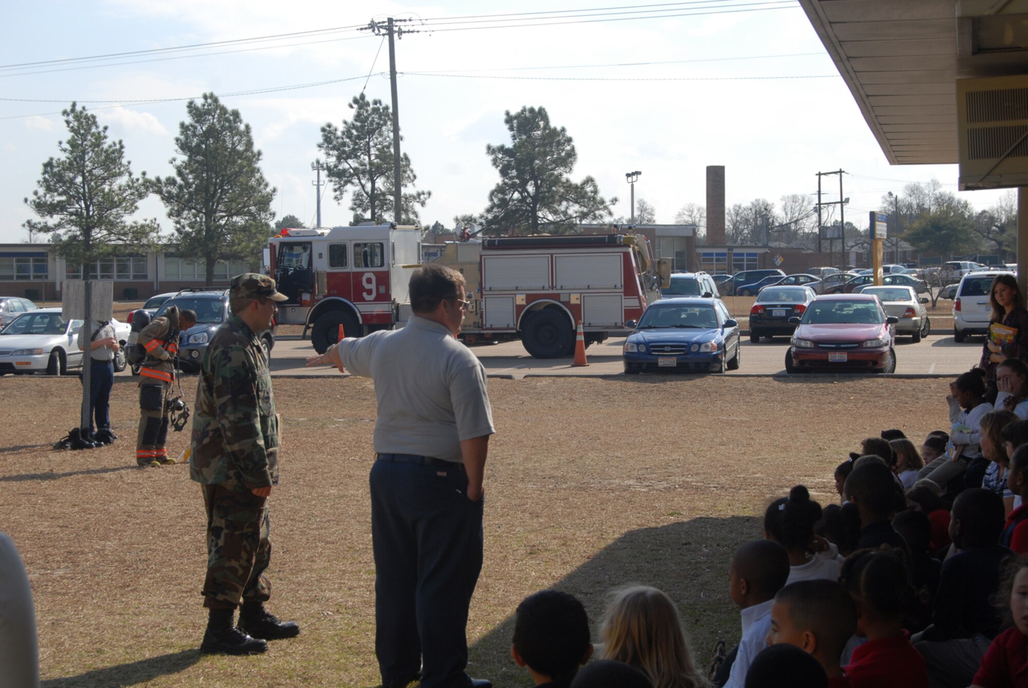(Right) Kurt Rhodes and Senior Airman Matthew Florez, Pope FIre Department, speak to students at Manchester Elementary School in Spring Lake, N.C. Feb. 5. In the background, Airman 1st Class Wendell Washington-Flournoy puts on his fire gear to show students there is nothing to be afraid of. (U.S Air Force Photo by 2nd Lt. Chris Hoyler)