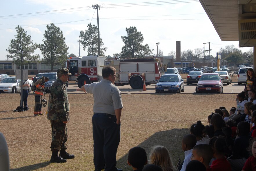 (Right) Kurt Rhodes and Senior Airman Matthew Florez, Pope FIre Department, speak to students at Manchester Elementary School in Spring Lake, N.C. Feb. 5. In the background, Airman 1st Class Wendell Washington-Flournoy puts on his fire gear to show students there is nothing to be afraid of. (U.S Air Force Photo by 2nd Lt. Chris Hoyler)