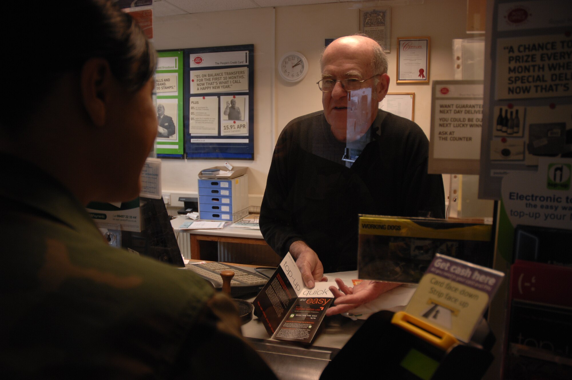 Mr. Leslie Hope, Sub Post Master of the British Post Office located on RAF Lakenheath, explains a top up plan for cell phones to Airman 1st Class Ashley Zamora, 48th Fighter Wing, Feb 15. The top up plan is one of many services offered to military members including paying British bills, internet and phone services and starting Feb 25th, the British Post Office will be able to exchange money between dollars and pounds. (U.S. Air Force photo by Senior Airman Brian J. Ellis)


