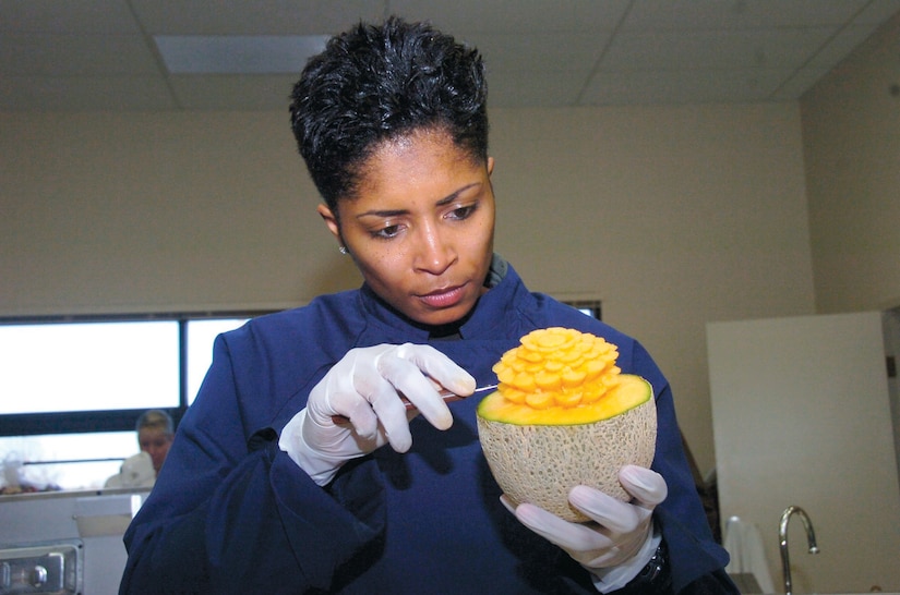 Master Sgt.  Monique Townsend, 89th Operations Group flight attendant, carefully sculps an intricate pattern on a cantalope to use with one of the centerpieces during a garnishing class.
(US Air Force/Bobby Jones)