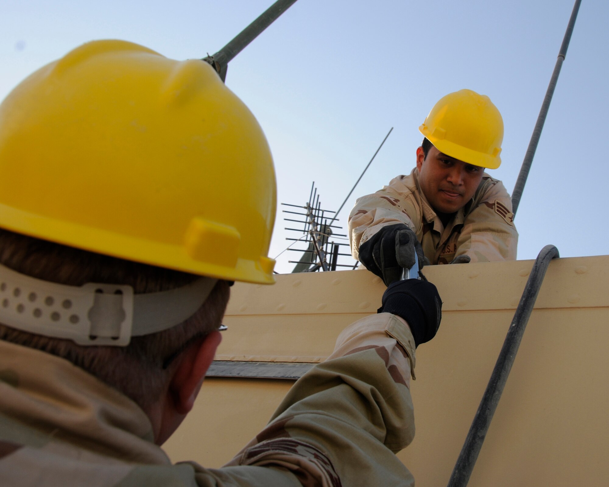 Tech. Sgt. Kenneth Paquin hands up a tool to his comrade, Senior Airman Arturo Vissarraga in process to repair a communications structure located inside the 71st Expeditionary Air Control Squadron compound Feb. 10. (U.S. Air Force photo/Senior Airman Domonique Simmons)