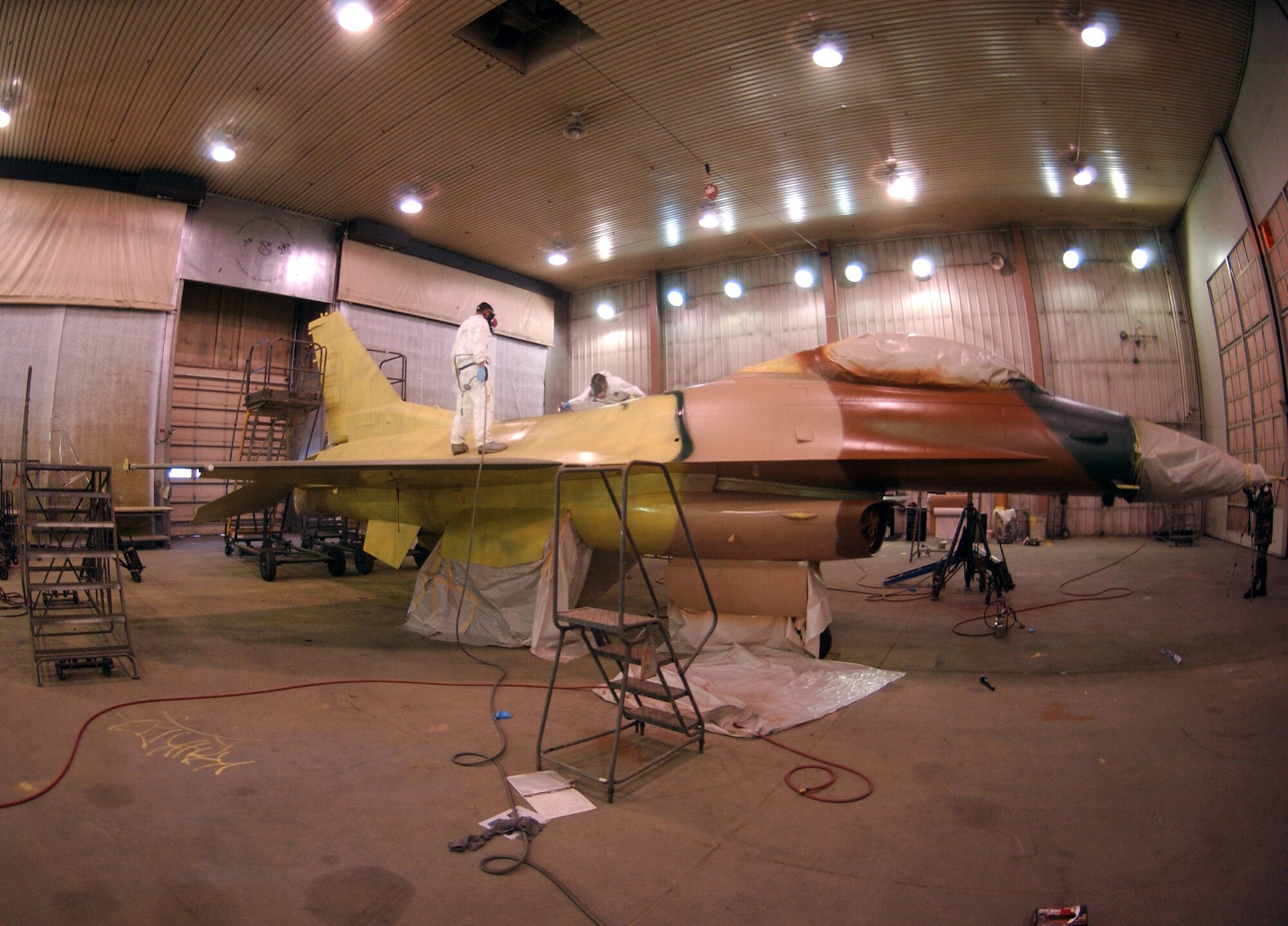 Senior Airman Frank Reardon and Airman 1st Class Eric Rickards apply a jungle theme to an F-16 Fighting Falcon Feb. 14 at the corrosion facility. With the swap of the F-16s from Kunsan Air Base, South Korea, to Eielson AFB in support of their new mission as aggressors, each aircraft is applied with a scheme being Arctic Flanker, Blue Flanker or a Lizard Flanker. Airmen Reardon and Rickards are 354th Maintenance Squadron sheet metal workers. (U.S. Air Force photo/Airman 1st Class Christopher Griffin)