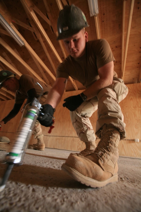 Seaman Jarred W. Jones, a utilitiesman with Naval Mobile Construction Battalion One, Detachment Al Taqaddum, applies a strip of adhesive to the floor of the new chapel at  Combat Outpost Ready. Once the glue was applied to the floor and the wood, the Seabees would carefully lay out the wooden flooring and weigh it down to ensure a tight seal. Jones is from Belpre, Ohio