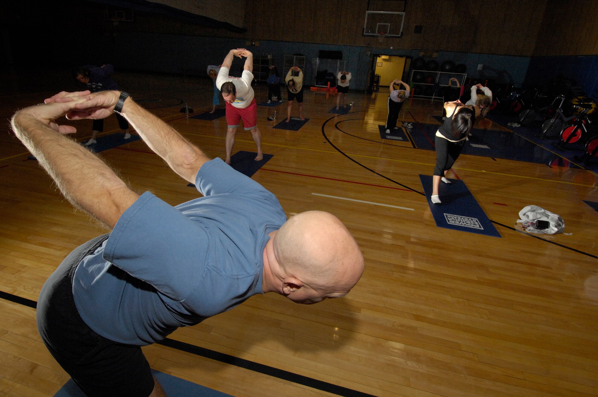 HANSCOM AFB, Mass. -- Charlie Harrington, a Yoga instructor, leads a group in stretches during a Yoga class Feb. 19 at the Fitness and Sports Center. The Fitness Center offers a variety of free classes for base personnel and their families. A few of the classes offered here include Power Funk, Boxing and Spinning. For a more comprehensive list of classes, visit www.hanscomservices.com, or contact the Fitness Center at (781) 377-3639. (U.S. Air Force photo by Mark Wyatt.)