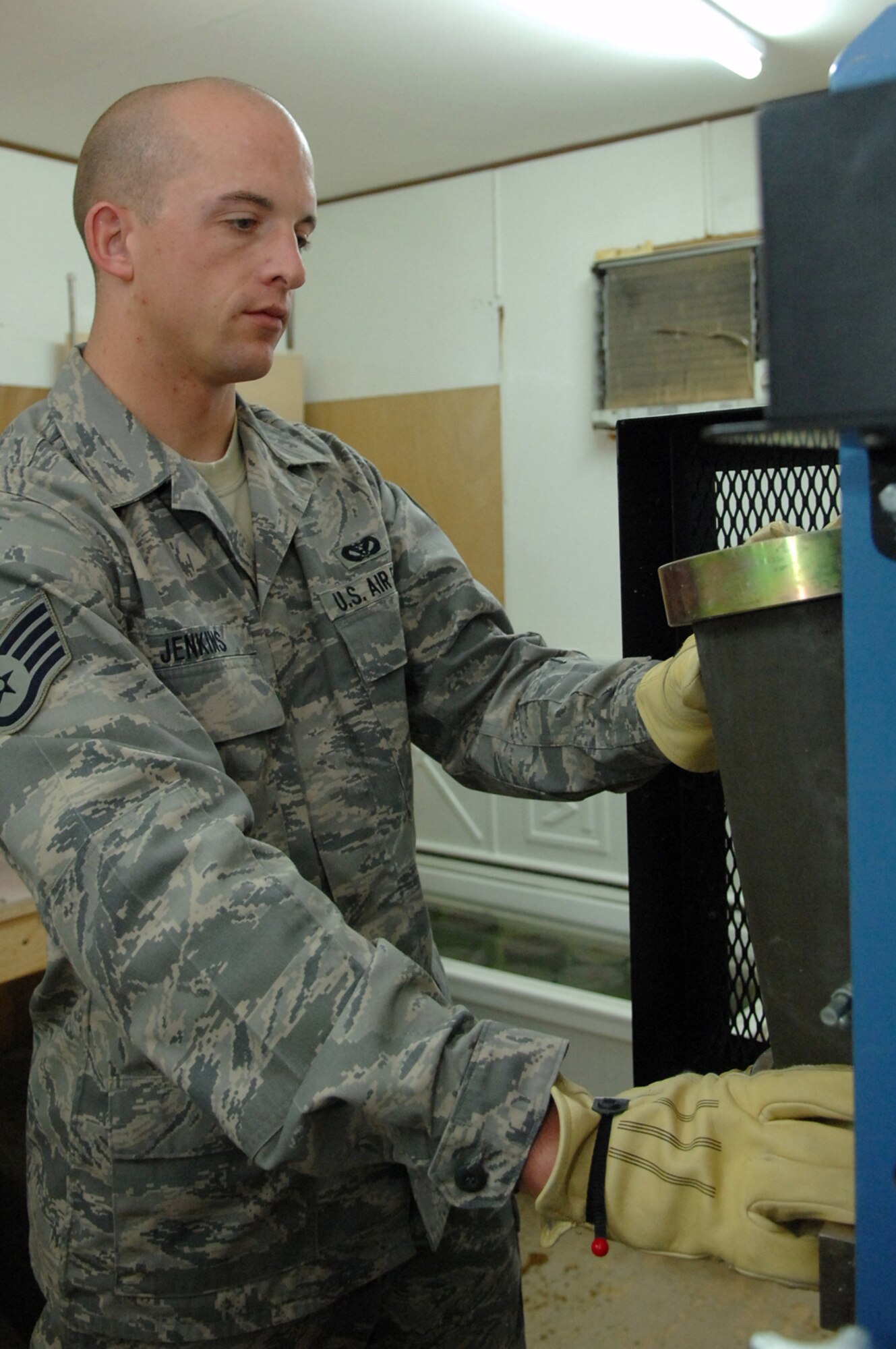 BALAD AIR BASE, Iraq -- Staff Sgt. Jack Jenkins, 332nd Civil Engineer Squadron engineering assistant, places a concrete cylinder sample, taken from the new Housing 6 area shoppette foundation, into a strength test machine here, Feb. 21. The machine will compress the sample until it breaks; to pass, the cylinder must withstand compression of 4,500 pounds per square inch. Sergeant Jenkins is deployed from Ellsworth Air Force Base, S.D. (U.S. Air Force photo/ Senior Airman Julianne Showalter)