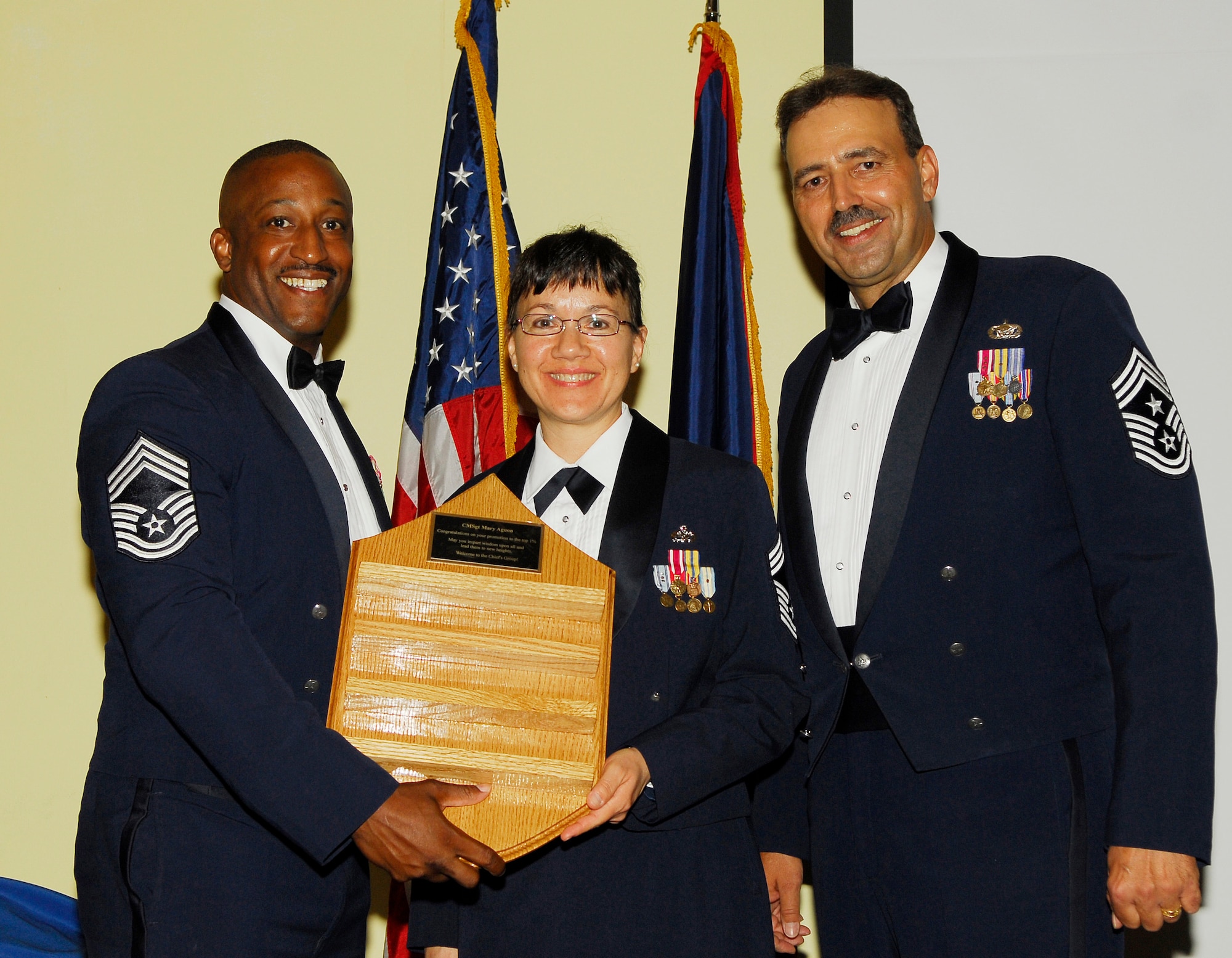 Chief Master Sgt. promotee Mary F. Aguon (center), 44th Aerial Port Squadron, recieves a chief chevron shaped coin holder from Chief Master Sgts. Vincent Eubanks (left), 36th Security Forces Squadron, and Saniford Andree (right), 36th Wing command chief master sergeant, during a chief induction ceremony Feb. 22. The plaque on it reads, "Congratulations on your promotion to the top 1%. May you impart wisdom  upon all around lead them to new heights. Welcome to the chief's group." (U.S. Air Force photo/Tech. Sgt. Michael Boquette)