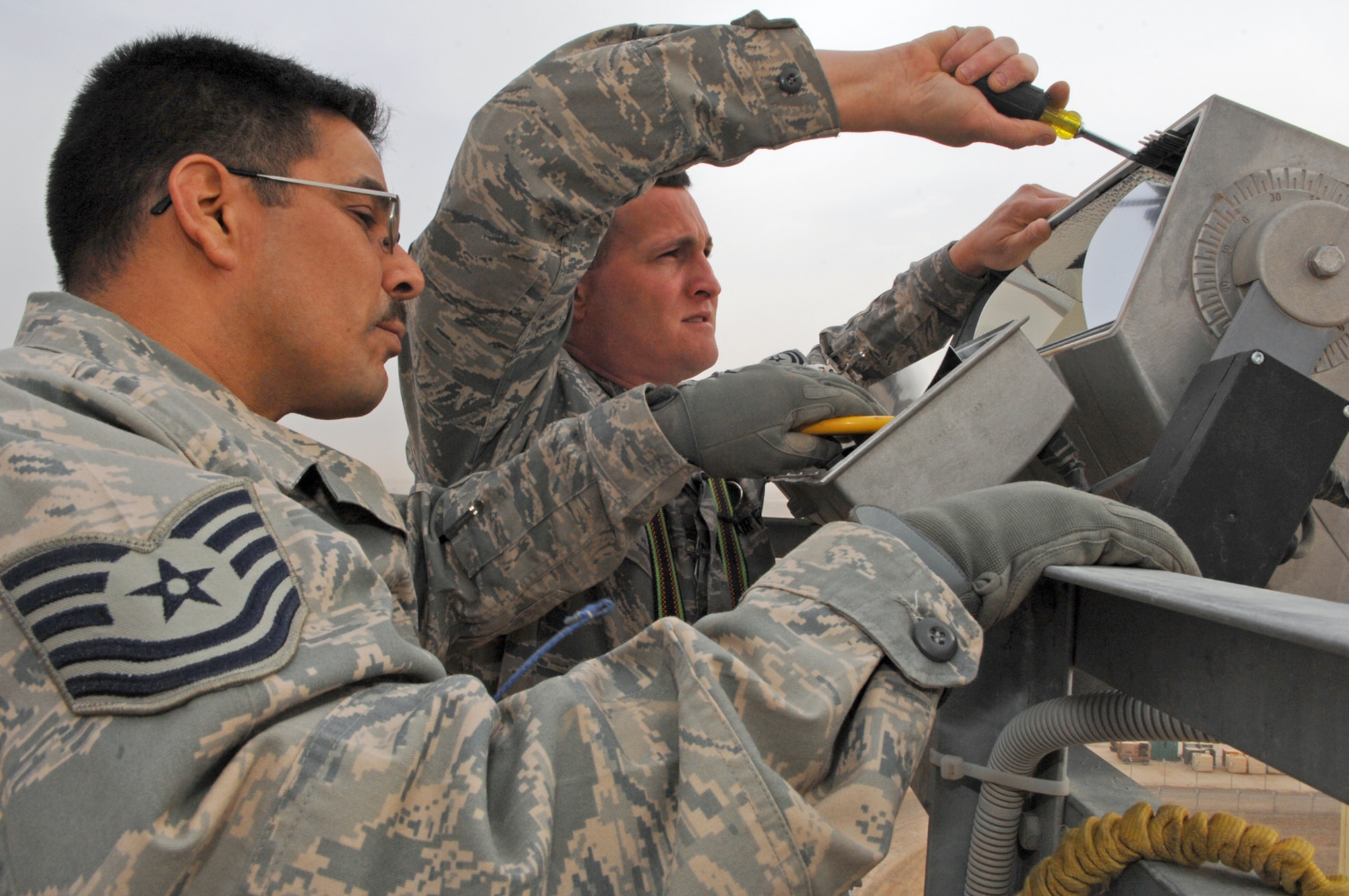 BALAD AIR BASE, Iraq -- Tech. Sgt. Ricardo Quevedo and Master Sgt. Mark Morgan, 332nd Expeditionary Civil Engineer Squadron electrical systems technicians, work together to fix a ballast transformer which powers a ramp-light here, Feb. 25. The technicians climbed a 100-foot tower to reach a broken light that illuminates a section of the flightline. Sergeant Quevedo is deployed from Luke Air Force Base, Ariz., and Sergeant Morgan is deployed from Eglin Air Force Base, Fla. (U.S. Air Force photo/ Senior Airman Julianne Showalter)