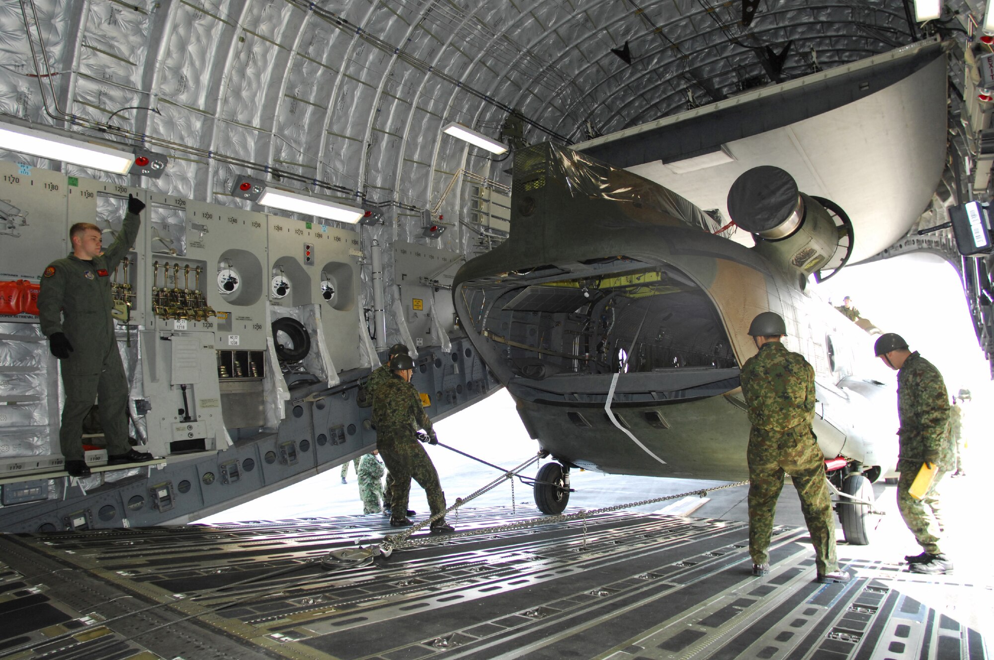 YOKOTA AIR BASE, Japan -- U.S. Air Force Staff Sgt. Ryan Boehm, left, directs the loading of a Japan Ground Self Defense Force CH-47J Chinook helicopter into a U.S. Air Force C-17 Globemaster III cargo plane Feb. 23. It was the first time a Japanese aircraft has been loaded into another nation's aircraft. The demonstration took place the last morning of the Pacific Global Air Mobility Seminar held Feb. 22 and 23. The CH-47J is assigned to the 1st Helicopter Brigade at JGSDF Camp Kisarazu in Kisarazu City, Chiba Prefecture.  Sergeant Boehm is a loadmaster assigned to the 535th Airlift Squadron, Hickam Air Force Base, Hawaii. The C-17 is also assigned to the 535th Airlift Squadron. (U.S. Air Force photo by Osakabe Yasuo)