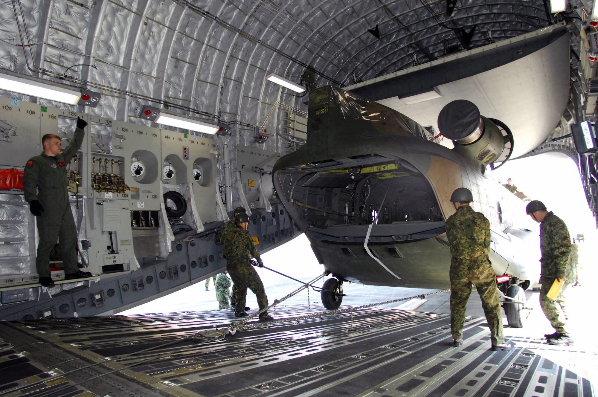 Staff Sgt. Ryan Boehm (left) directs the loading of a Japan Ground Self Defense Force CH-47J Chinook onto a C-17 Globemaster III cargo plane Feb. 23 at Yokota Air Base, Japan. The demonstration was conducted during the Pacific Global Air Mobility Seminar held Feb. 22 and 23. The CH-47J is assigned to the 1st Helicopter Brigade at JGSDF Camp Kisarazu in Kisarazu City, Chiba Prefecture. Sergeant Boehm is a loadmaster assigned to the 535th Airlift Squadron at Hickam Air Force Base, Hawaii. The C-17 is also assigned to the 535th Airlift Squadron. (U.S. Air Force photo/Osakabe Yasuo) 
