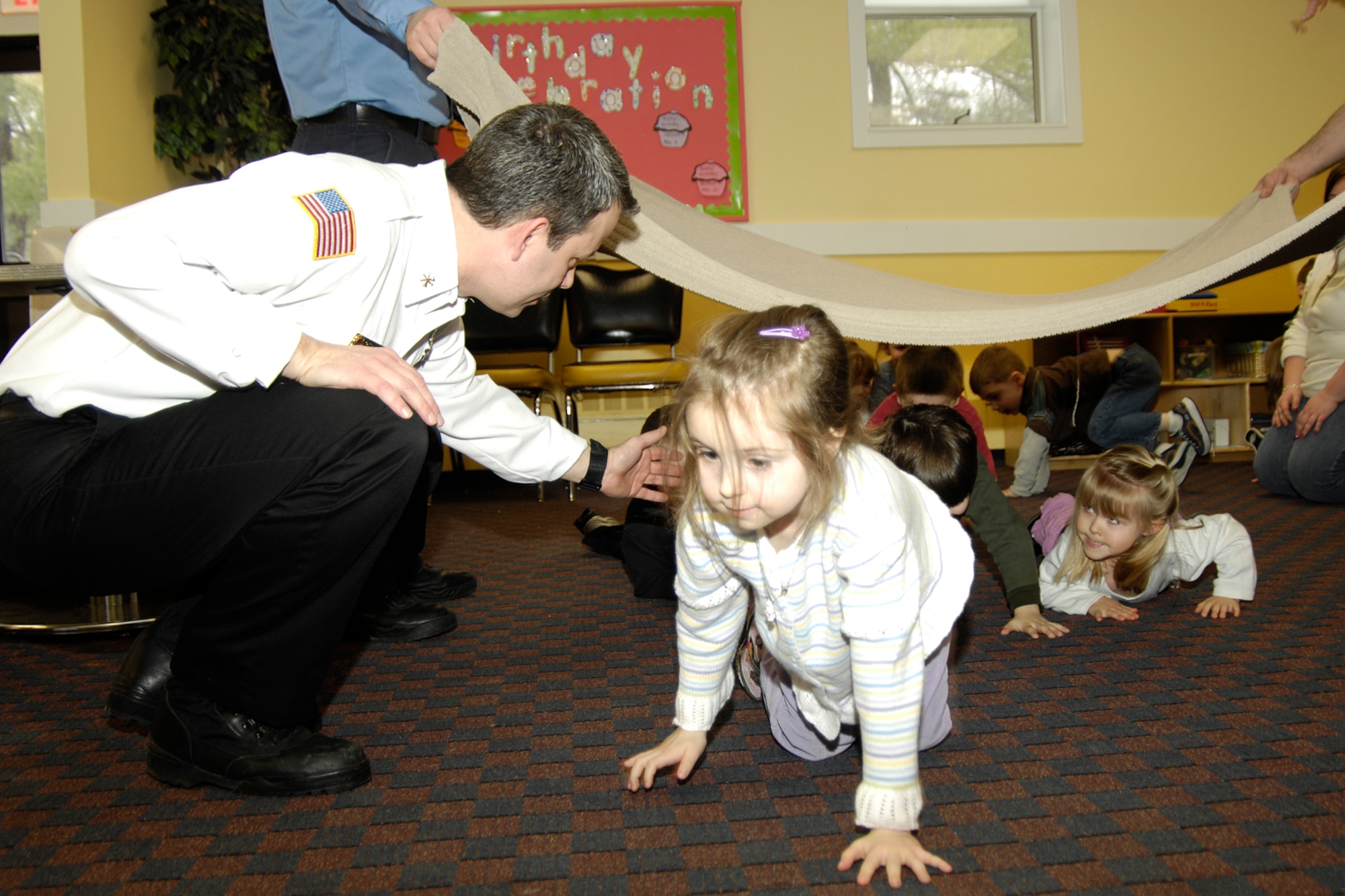 HANSCOM AFB, Mass. – Robert Coonce (left), Hanscom Fire Prevention Services and assistant fire chief, guides Elena Weissman (right) and other children from the Hanscom School Age program through a drop and crawl drill designed to teach children how to safely get out of a smoke-filled house. The interactive exercise was part of a new Juvenile Fire Setters program that the Fire Department unveiled Feb. 26. (U.S. Air Force photo by Linda LaBonte Britt)

