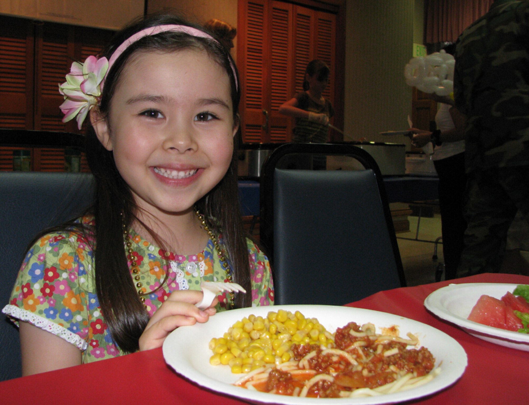 One of the youngest volunteers, Ivy, a daughter of Jacqueline Mach, from Hickam Nelles Chapel enjoys her meal after contributing her service to the monthly activity dinner