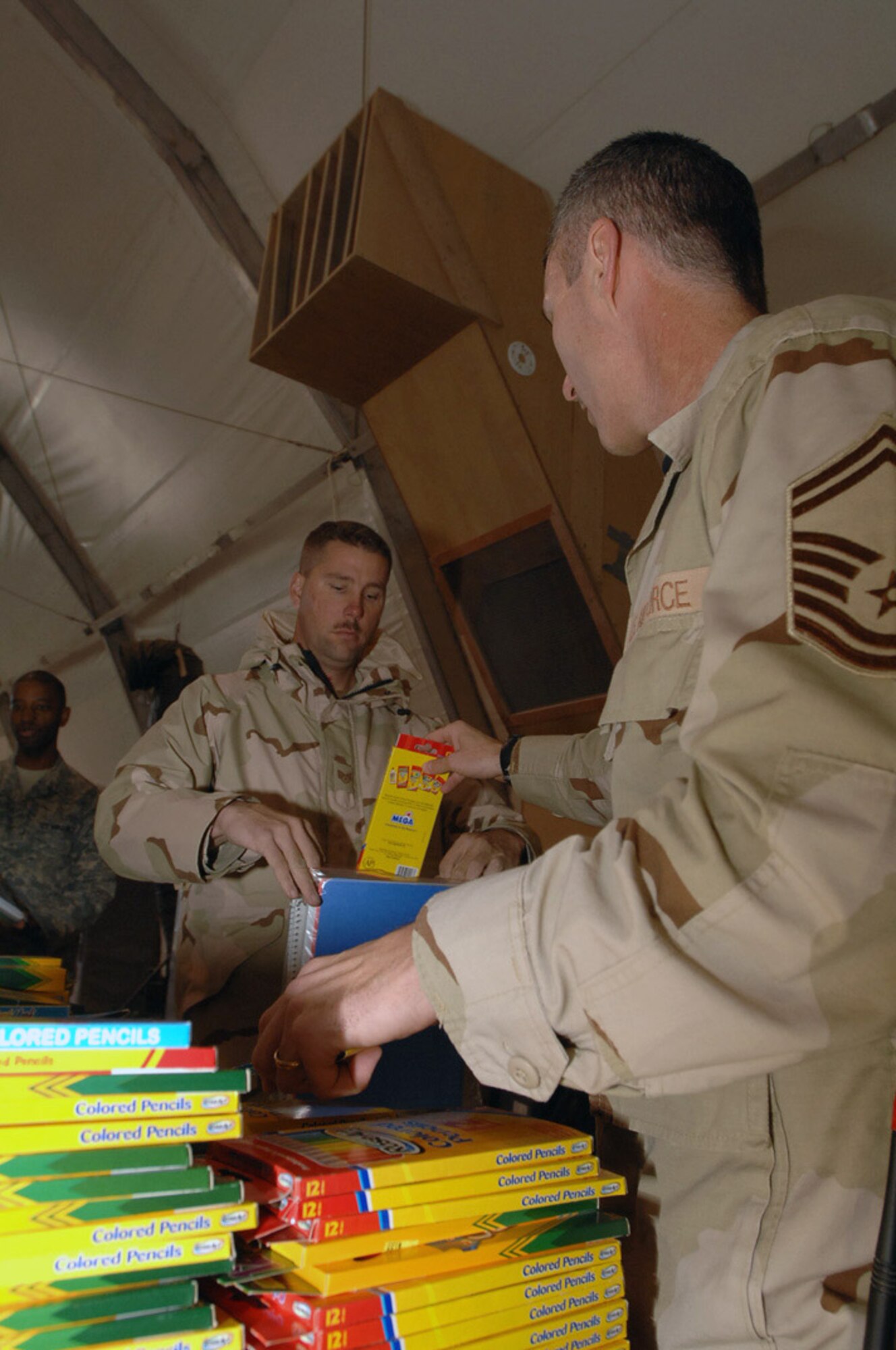 Senior Master Sgt. Vincent Marler drops colored pencils into Staff Sgt. Bobby Siers' bag of school supplies at Ali Base, Iraq,Dec. 22. The Airmen are sorting through donated school supplies in support of Operation Iraqi Child led by the 407th Air Expedtionary Group Focus 5/6 and Top 3 councils. In just over a month, Airmen on base collected thousands of school supply items, soccer balls, stuffed animals and toys. The donated items will be given to Iraqi families in the An Nasiriyah area villages. Sergeant Marler is assigned to the 407th Expeditionary Operations Support Squadron and is deployed from Whiteman Air Force Base, Mo. Sergeant Siers is assigned to the 407th Expeditionary Civil Engineer Squadron and is deployed from Hickam AFB, Hawaii. (U.S. Air Force photo/Airman 1st Class Jonathan Snyder) 