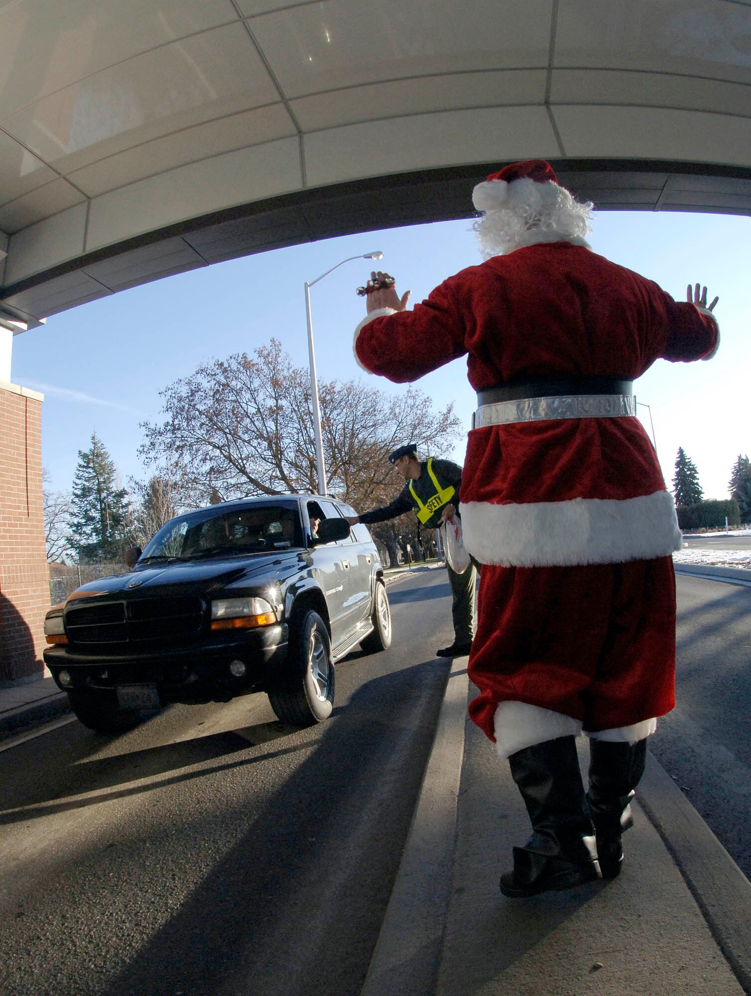 FAIRCHILD AIR FORCE BASE, Wash. – Santa Claus waves to in and outbound traffic at the main gate Dec. 21 as he wishes happy holidays and passes out candy canes to drivers and passengers. Col. Thomas Sharpy, 92nd Air Refueling Wing commander, squadron commanders and various personnel participated in the event. (U.S. Air Force photo /Staff Sgt. JT May III)