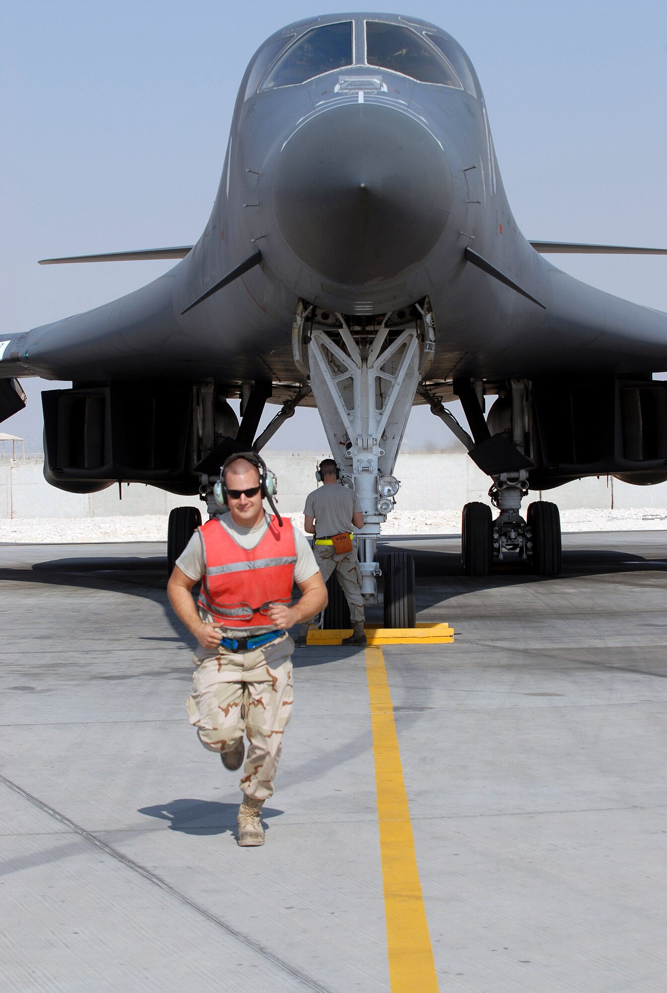 Senior Airman Ryan Bathke runs to his position to marshal a B-1B Lancer bomber to the taxiway for a mission Dec. 29 as Senior Airman Nathan Konkol, waits at the nose gear to pull the chocks. The Airmen are with the 379th Expeditionary Aircraft Maintenance Squadron at an air base in Southwest Asia.  (U. S. Air Force photo/Staff Sgt. Douglas Olsen)
