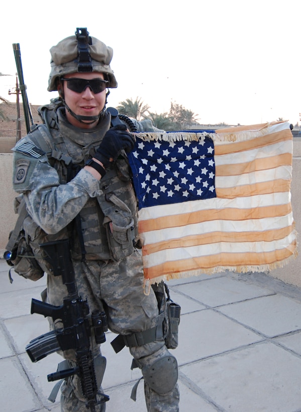 Army Pfc. Alexander Cesario, of Somerville, N.J., a forward observer with Company A, Special Troops Battalion, 2nd Brigade Combat Team, 82nd Airborne Division, displays his father's American flag on a rooftop in Baghdad's Suleikh neighborhood, Dec. 27, 2007. As a soldier in Vietnam, the elder Cesario flew the flag every day -- including a three-day period that he was missing in action -- and his son now carries it with him on patrols in Iraq. Photo by Staff Sgt. Mike Pryor, USA 