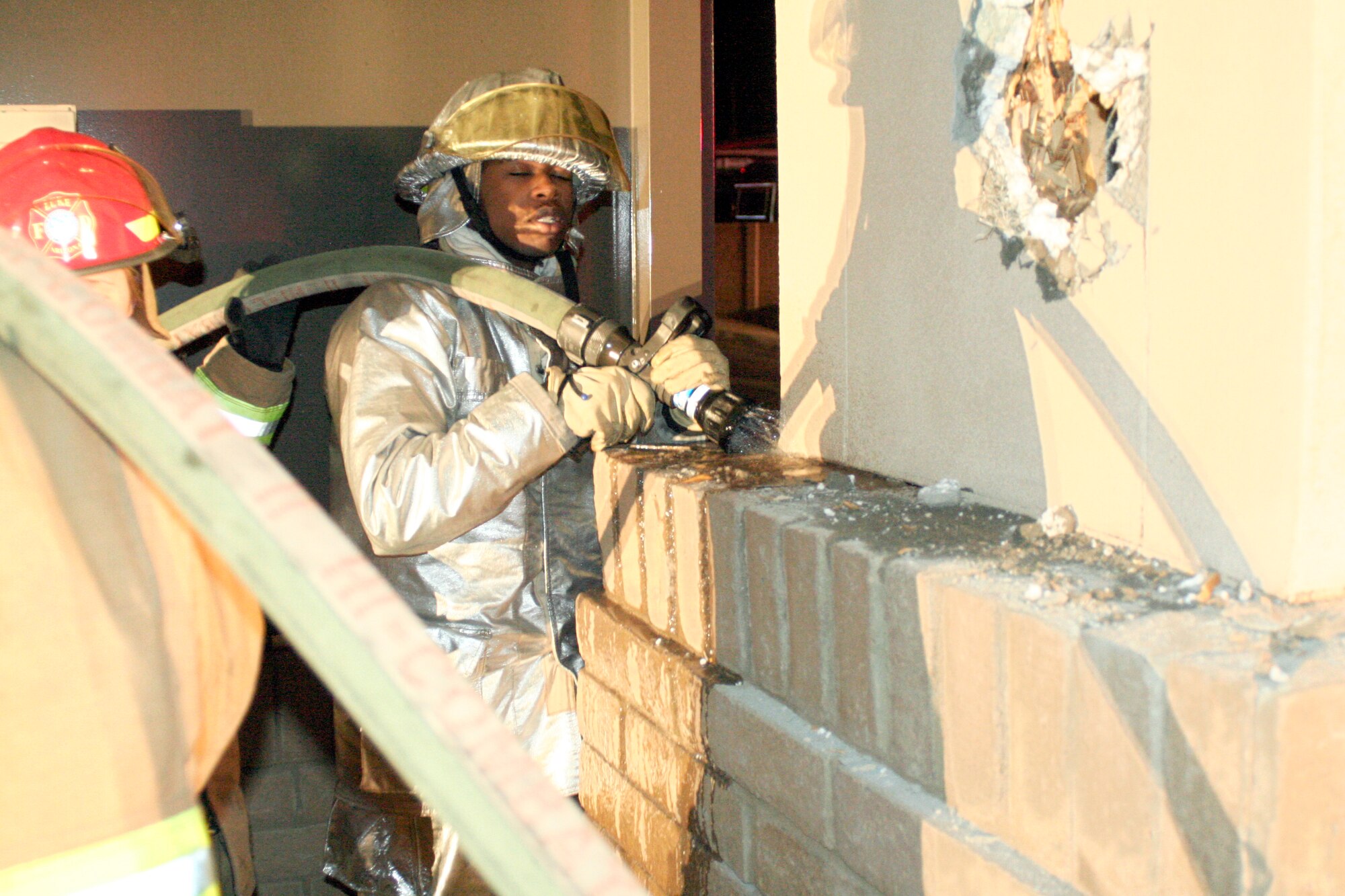 Airman 1st Class Thomas Brooks (right) and Cyndi Belcher (red helmet) and other members of the base fire department work to put out a small fire smoldering at the North Gate Dec. 22. While many Thunderbolts enjoyed well-deserved time off over the holidays, the fire department, security forces, command post and other members of Luke worked to keep the base safe. (photo by Airman 1st Class C.J. Hatch)