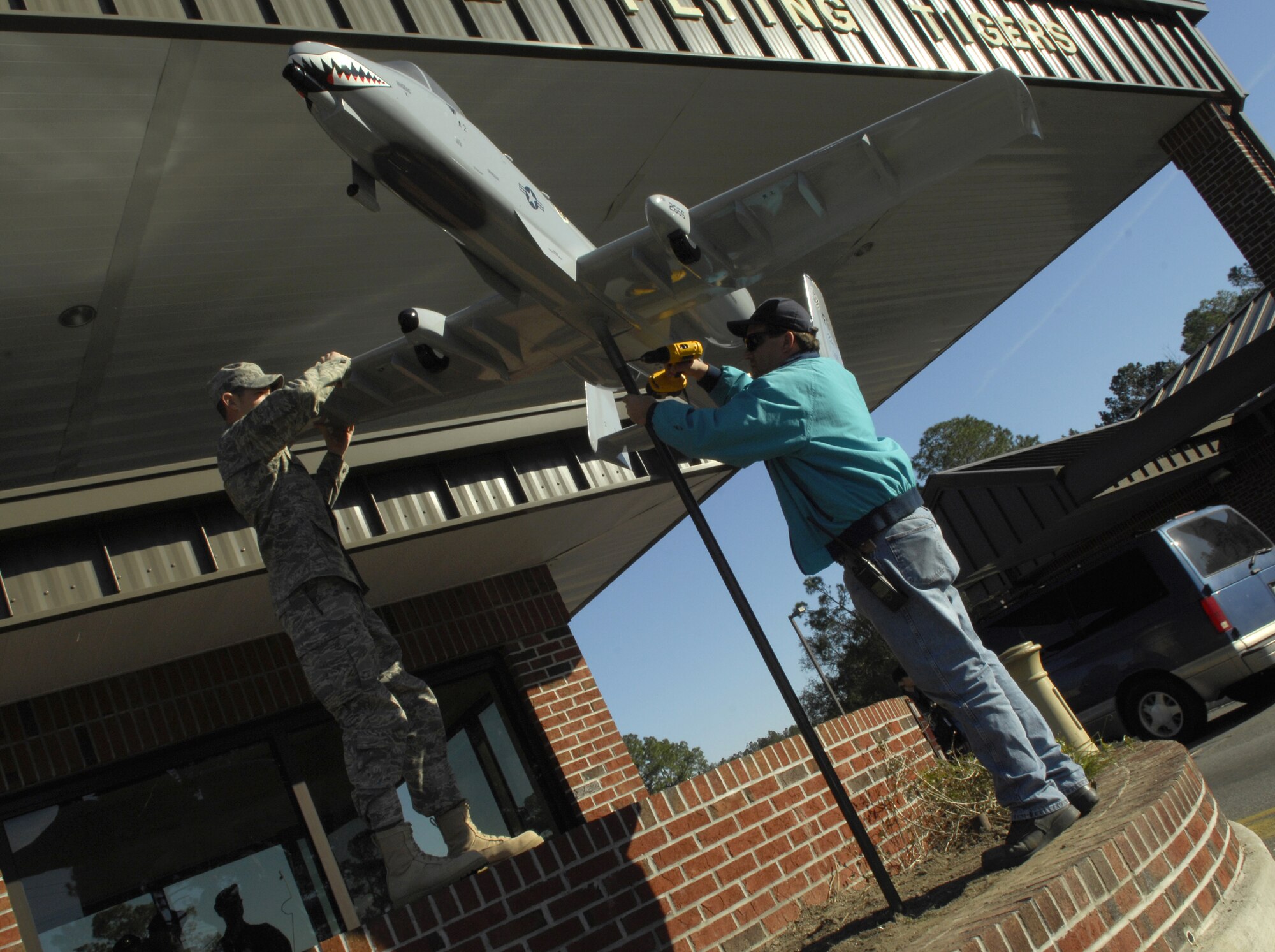 Staff Sgt. Jonathan Morgan and Jeffrey Hendricks, 23rd Civil Engineer Squadron, secure a scale model of an A-10C Thunderbolt ll at the South Gate here Jan 3. The aircraft model was added to represent the addition of the 23rd Fighter Group to Moody's mission. (U.S. Air Force Photo by Senior Airman Elizabeth Rissmiller)