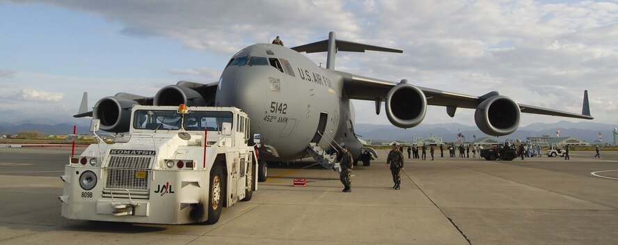 A C-17 in Komatsu, Japan is having its cargo off-loaded by Japanese airport workers after being pushed into its parking spot by the vehicle in the foreground. The 729th Airlift Squadron, March Air Reserve Base, was picking up an F-15 squadron from Kadena and deploying their equipment to Komatsu for an exercise this past October. (Courtesy photo)