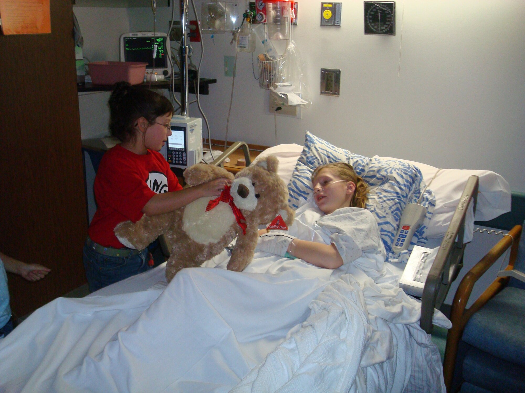 Jaila Suarez of the Air Force Academy's Falcon Trail Youth Center presents a teddy bear to 11-year-old Claire Ruth, a patient in the Penrose Community Hospital Pediatrics Department Dec. 20. Children at the youth center delivered more than 160 teddy bears to the Pediatrics Department as part of the Child Care Connections, Inc., "Teddy Bears for Kids" Program. Staff Sgt. Thomas Moore, assigned to the Space Missile Systems Center at Peterson AFB, Colo., started the program five years ago and has been spearheading the community project every year since then. (Courtesy photo)