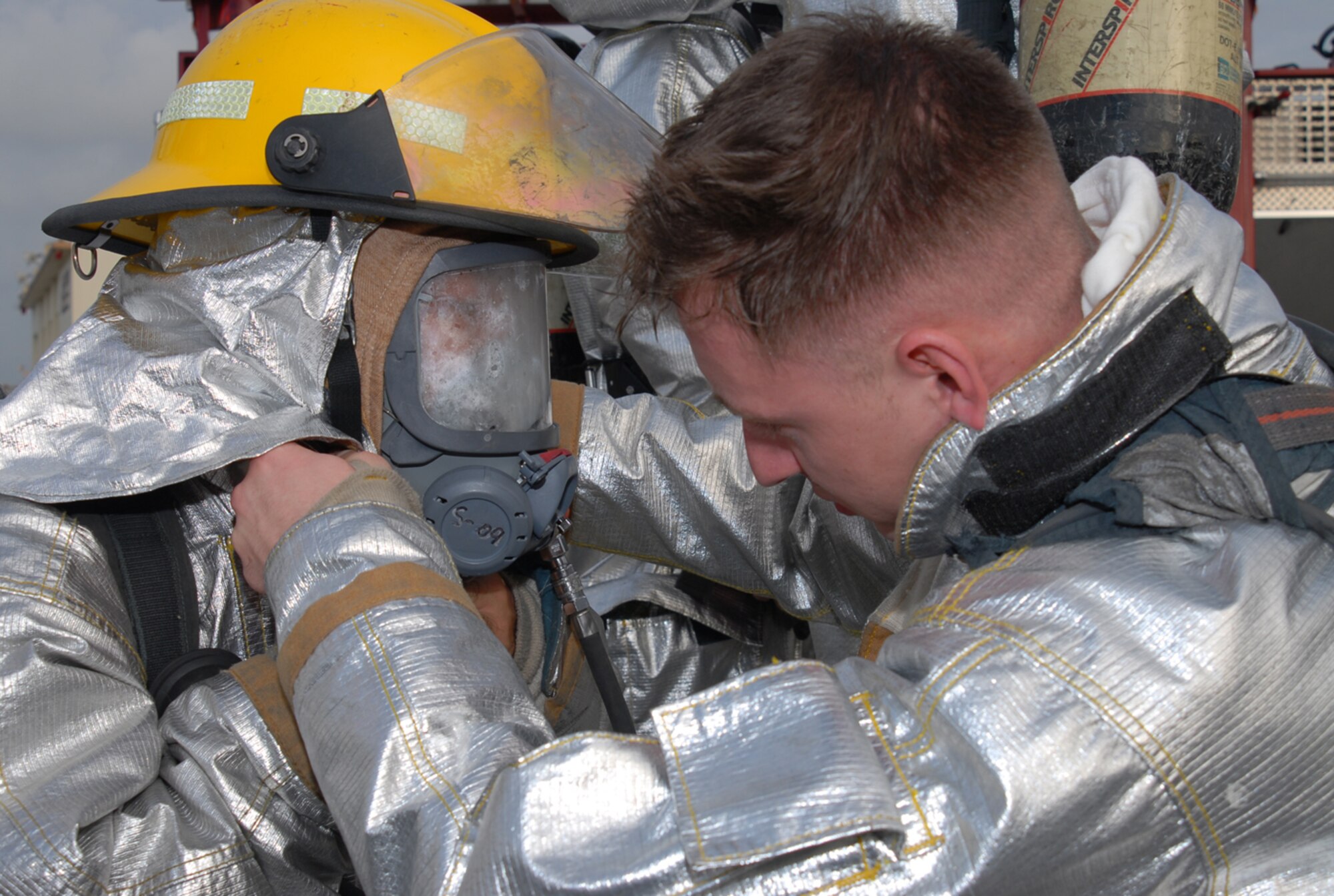 Airman 1st Class Matt Mical, 18th Civil Engineer Squadron, helps a fellow firefighter put on a gas mask following a simulated fuel spill scenario during Local Operational Readiness Exercise Beverly High 08-3 at Kadena Air Base, Japan, Jan. 7, 2007. The 18th Wing exercise from Jan. 7 to 11 tests the wing's ability to respond in contingency situations. (U.S. Air Force photo/Tech Sgt. Dave DeRemer)