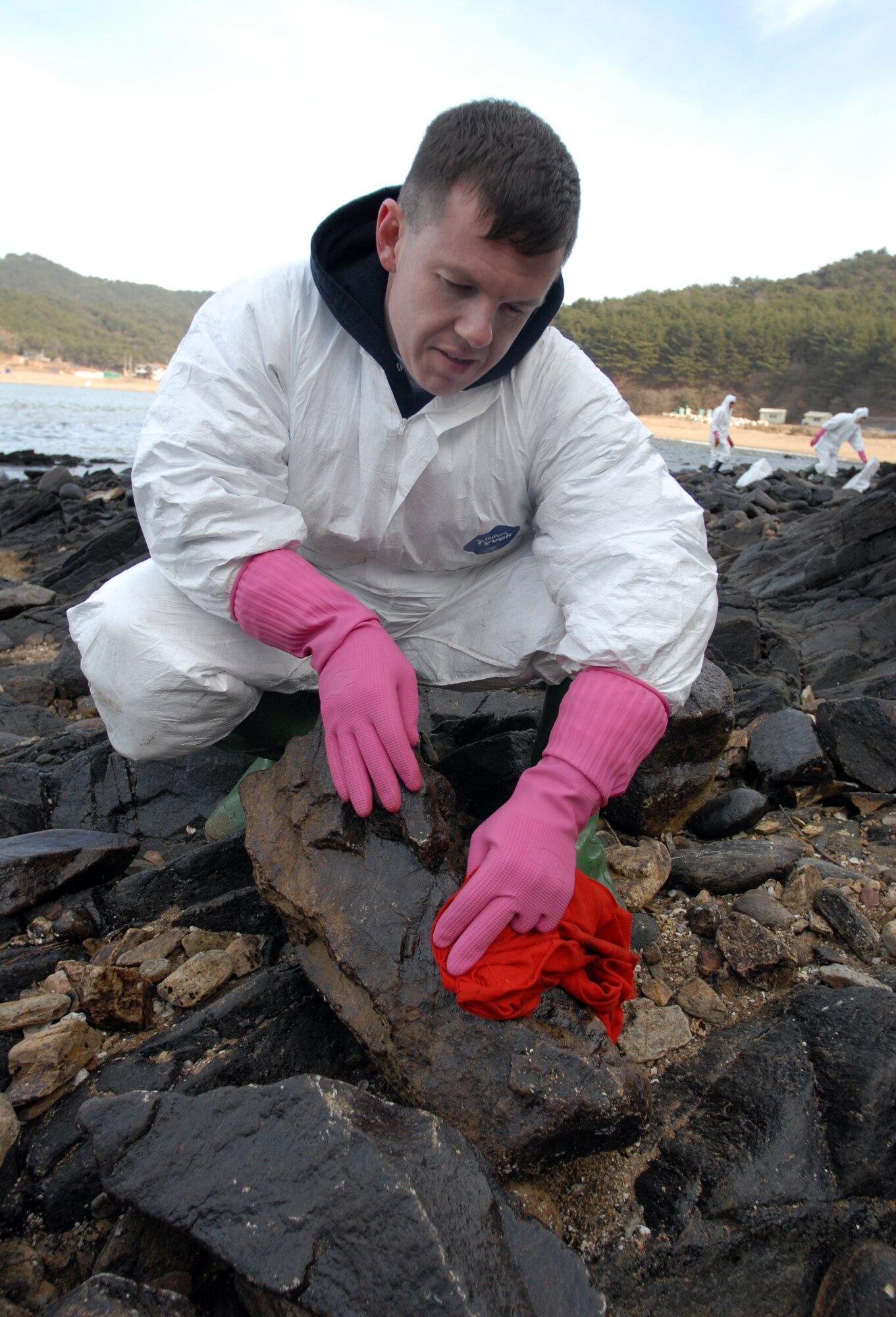 MALLIPO BEACH, South Korea -- Technical Sgt. Jason Rosenbaum, a fireman with the 8th Civil Engineer Squadron, Kunsan Air Base, cleans a rock after crude oil spilled from a crane barge December 7, 2007 and washed ashore here. Over 200,000 volunteers assisted with the clean up of 2.7 million gallons of oil.  Several agencies, to include 13 helicopters, 17 airplanes, 327 vessels and United States Air Force, Army and Korean nationals took part in the clean up efforts. (U.S. Air Force photo/Senior Airman Steven R. Doty)