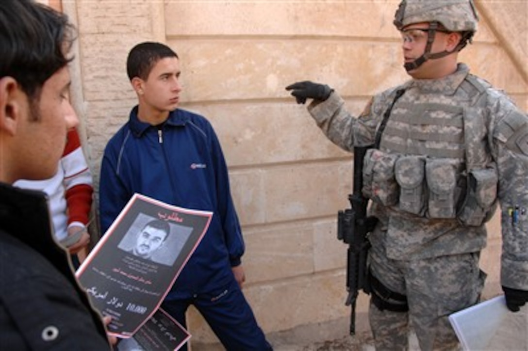 Sgt. Sam Talley talks to young Iraqi men as he passes out wanted posters during a patrol in Mosul, Iraq, on Dec. 30, 2007.  Talley is attached to the U.S. Army's Tactical Psychological Operation Detachment 1400.  