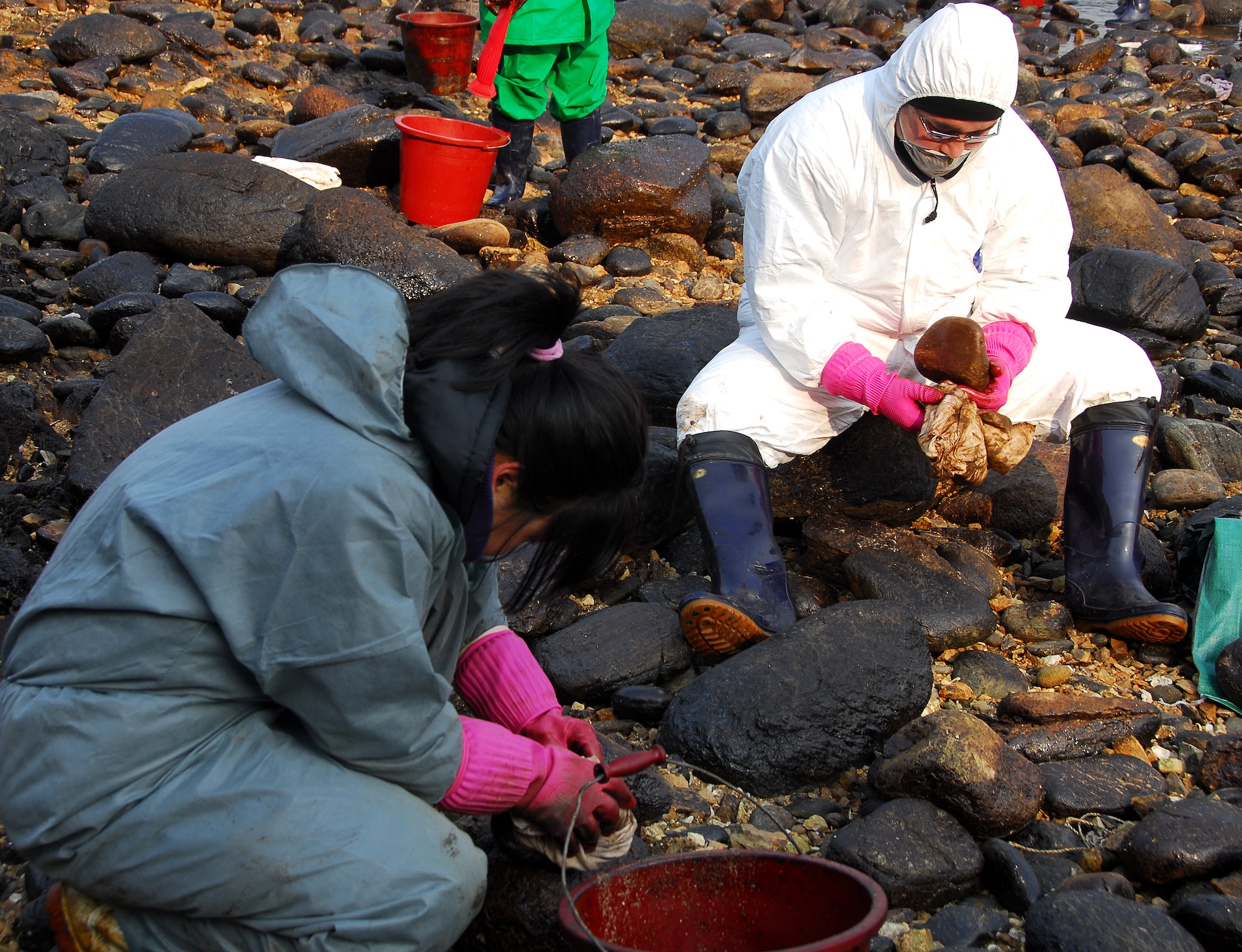Taean, Republic of Korea -- A Korean and an Airman from Osan Air Base clean oil-stained rocks Thursday on the beach near Taean City after the worst oil spill in South Korean history.  Hundreds of American military personnel have joined the hordes of volunteers along local coastlines who are assisting with the clean-up effort.  (U.S. Air Force Photo by Senior Airman Chad Strohmeyer) 
