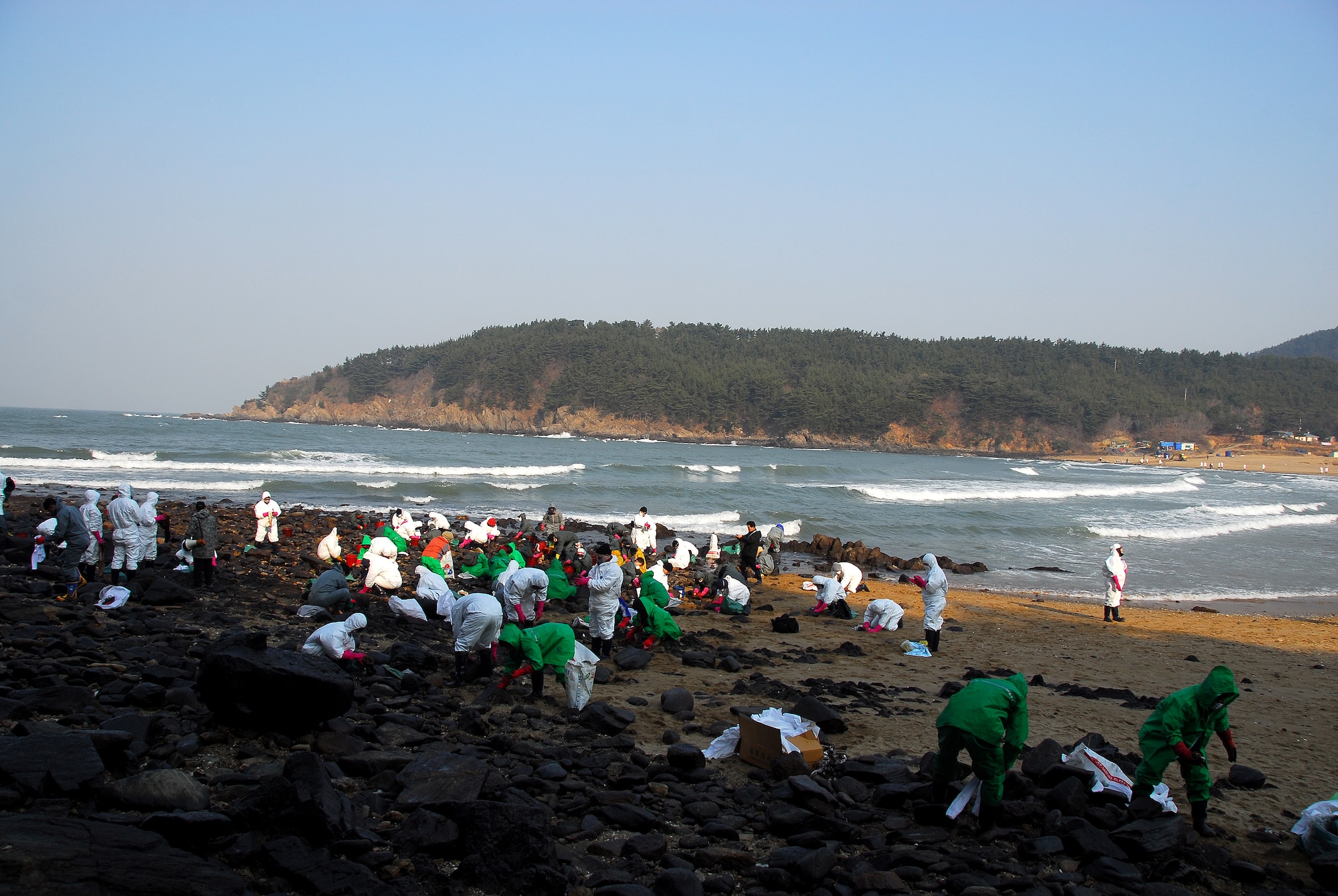 Taean, Republic of Korea -- United States Air Force Airmen from Osan Air Base work side by side with hundreds of Koreans Thursday to clean oil-stained rocks on the beach near Taean City. After the largest crude oil spill in the history of the region, hundreds of American military personnel have joined the hordes of volunteers along local coastlines who are assisting with the clean-up effort.  (U.S. Air Force Photo by Senior Airman Chad Strohmeyer) 
